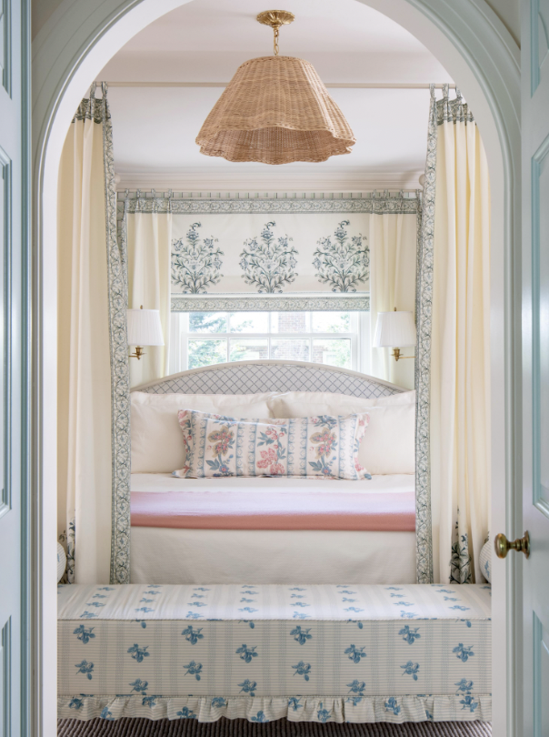 A cozy bedroom seen through an arched doorway with a built-in window seat, floral patterns, and soft pastel colors created by interior designer Jenny Holladay Design who's based in Richmond, VA.