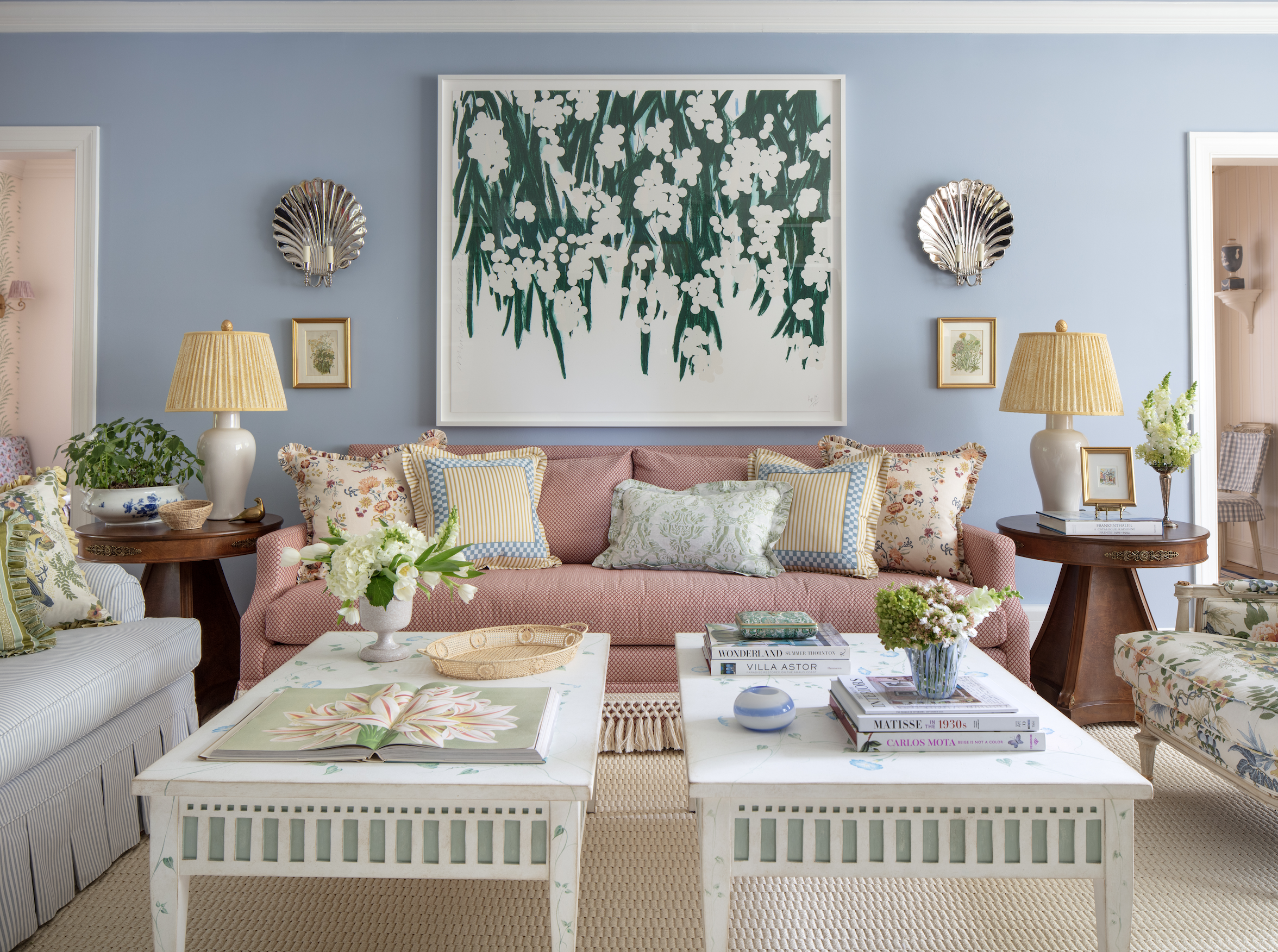 Living room with pastel blue walls, floral and striped pillows, two side tables with lamps, and a large framed botanical painting on the wall created by interior designer Jenny Holladay Design who's based in Richmond, VA.