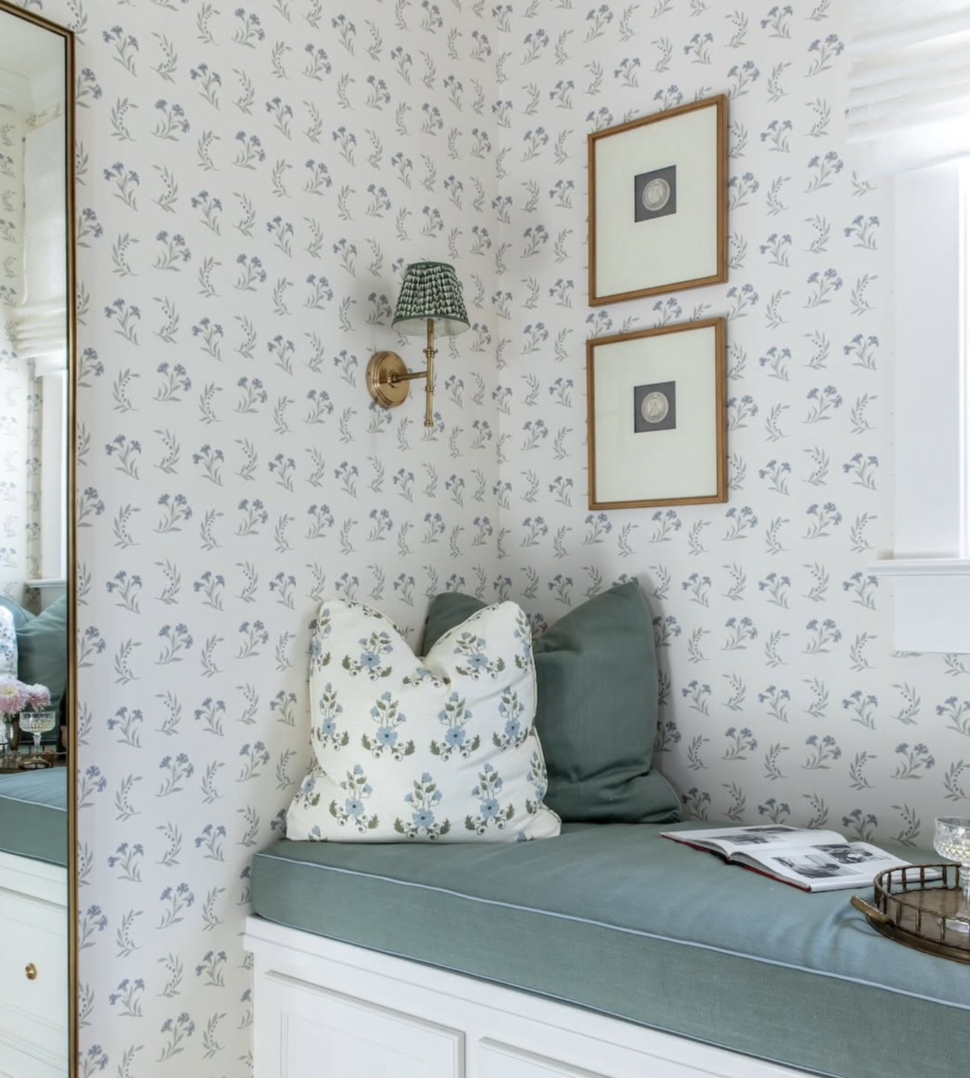A cozy window nook with floral wallpaper, a brass wall sconce with a patterned shade, and framed artwork created by Richmond, VA interior designer Jenny Holladay Design.