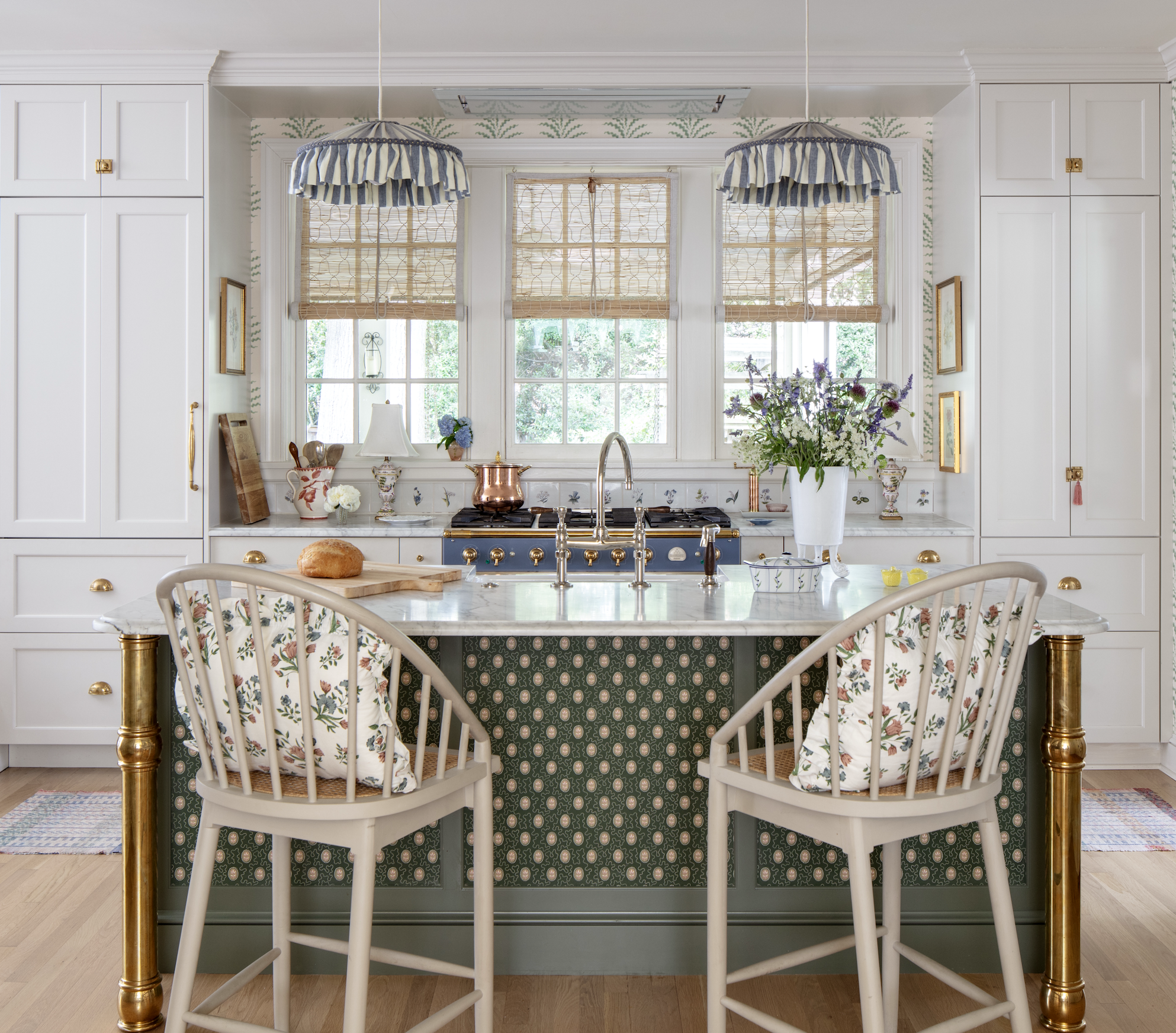 A kitchen with white cabinetry, a marble countertop, and a window with wooden blinds. There are two blue and white striped pendant lamps hanging above the counter created by interior designer Jenny Holladay Design who's based in Richmond, VA.