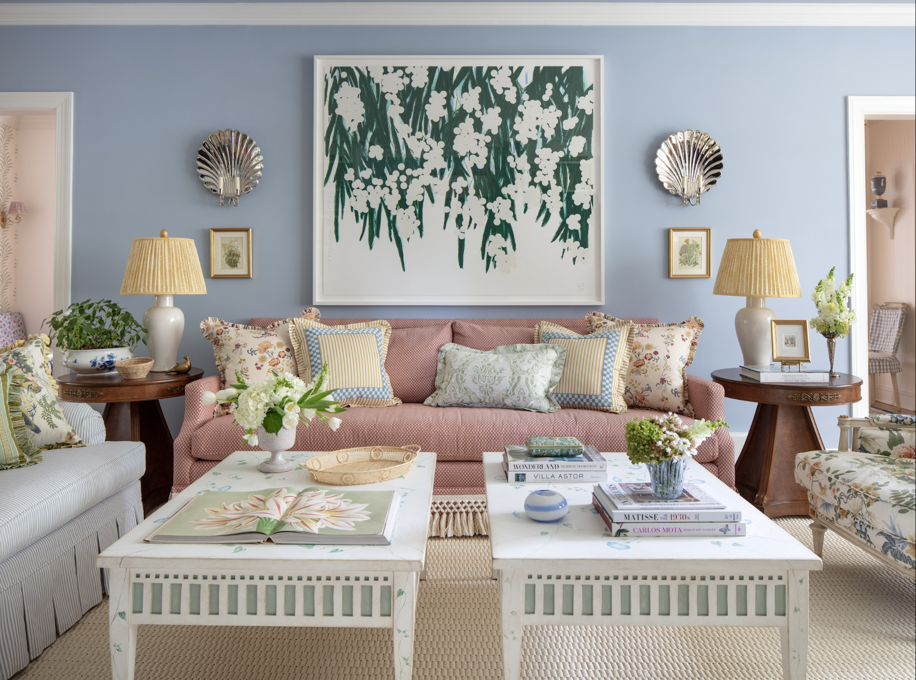 Living room interior with pastel pink sofa, white coffee table with magazines and floral arrangements, side tables with lamps, gold framed artwork created by Jenny Holladay Design, interior designer based in Richmond VA.