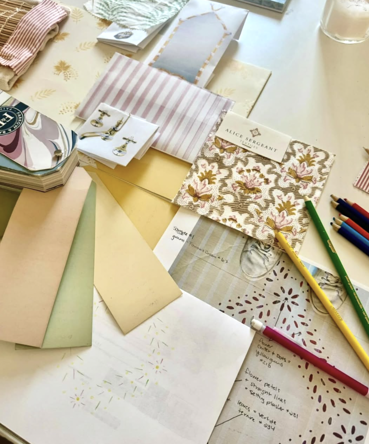 A table covered with various fabric swatches, colored pens, and fashion sketches of floral and stripe patterns, along with some jewelry and design notes.