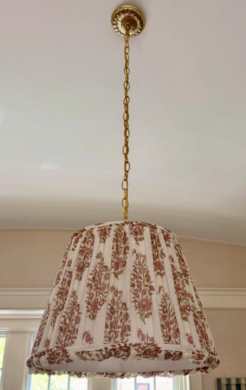 A hanging pendant lampshade with a floral pattern in shades of pink and green on a beige background, attached to a gold chain and ceiling fixture.