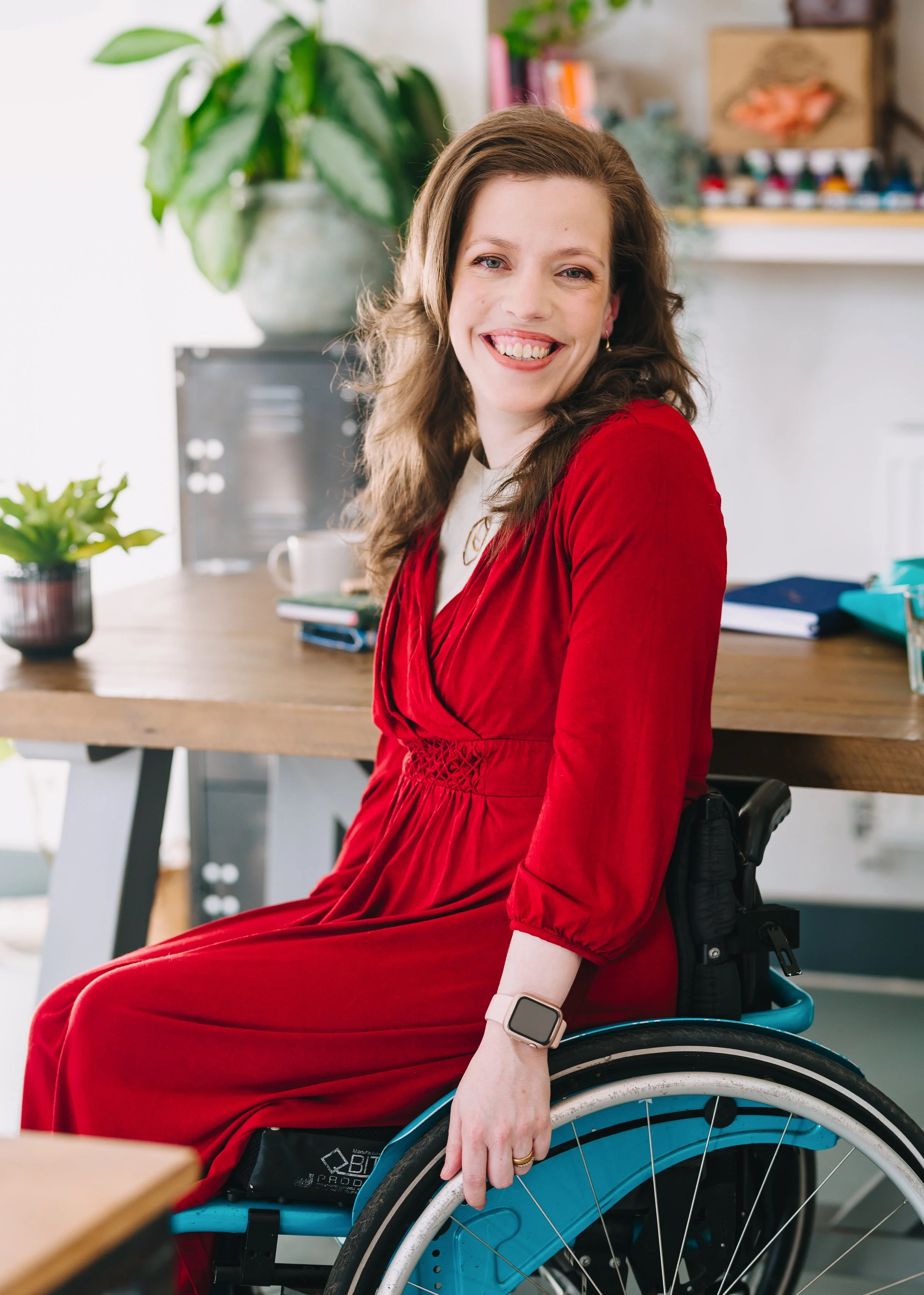 Grace Quantock in a red dress and on a teal wheelchair in an office, smiling