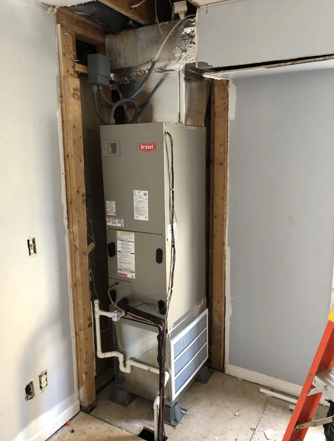 Installation of a new HVAC furnace in a home, with exposed wall framing, electrical wiring, and a ladder nearby.