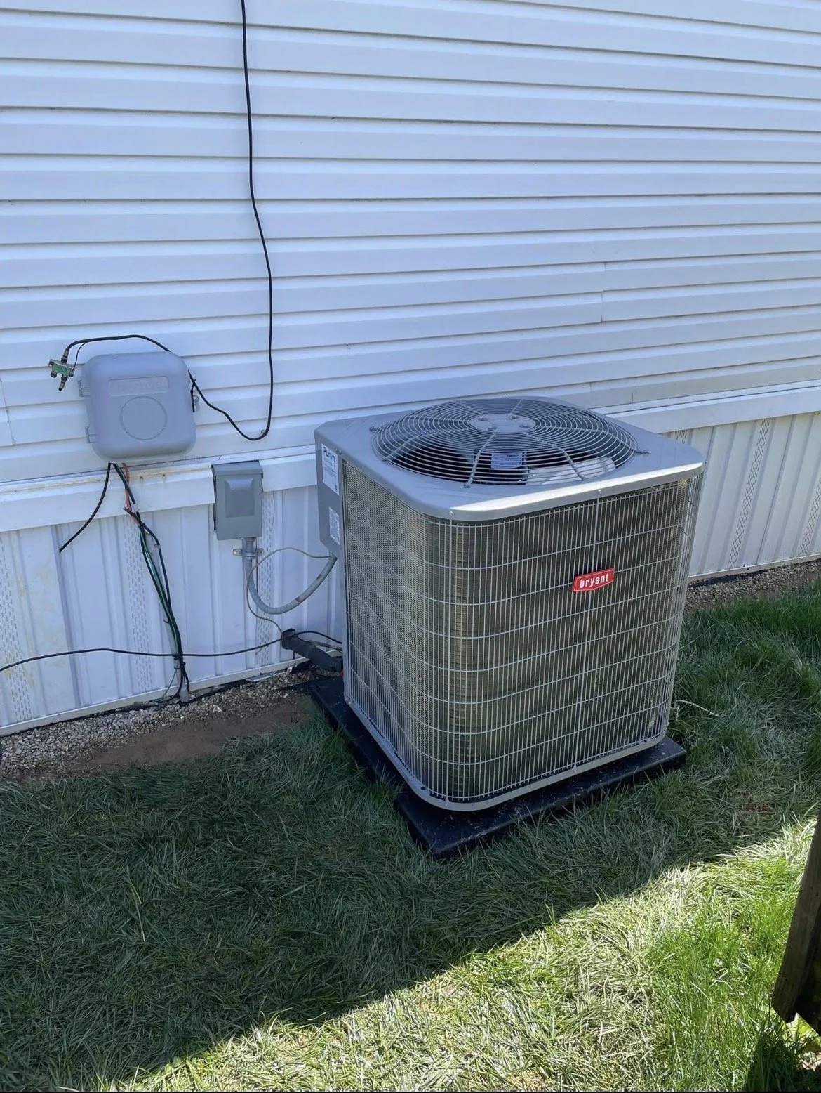 An outdoor air conditioning unit with a Bryant logo next to a white wall with electrical wiring and meters.