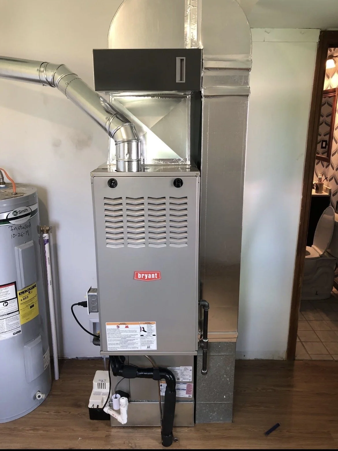 A Bryant furnace unit installed in a home's basement, with ductwork connected to the top, and a water heater to the left.