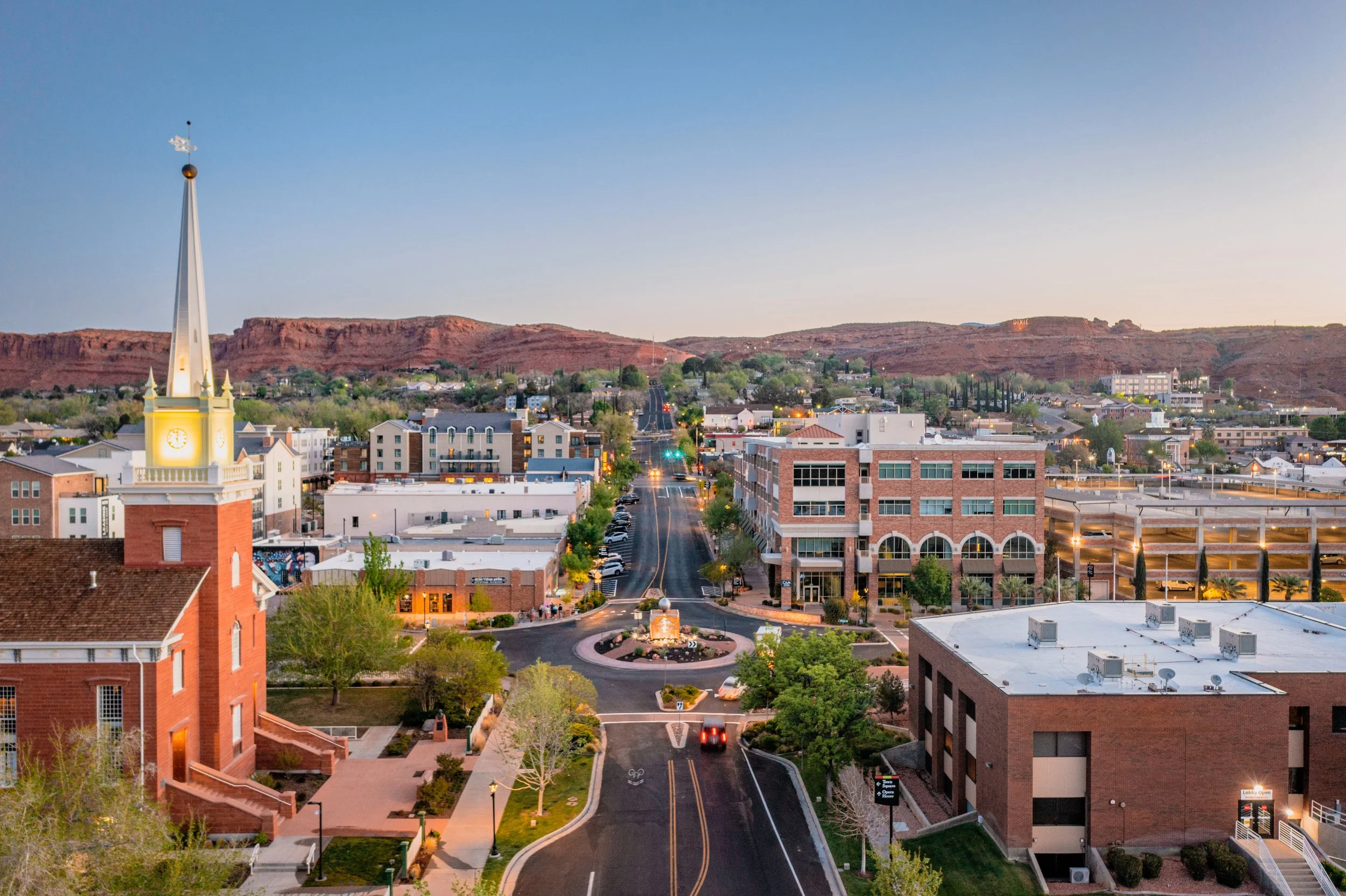 A scenic view of Utah with residential and commercial buildings, a street with cars, and a mountain range in the background during dusk.