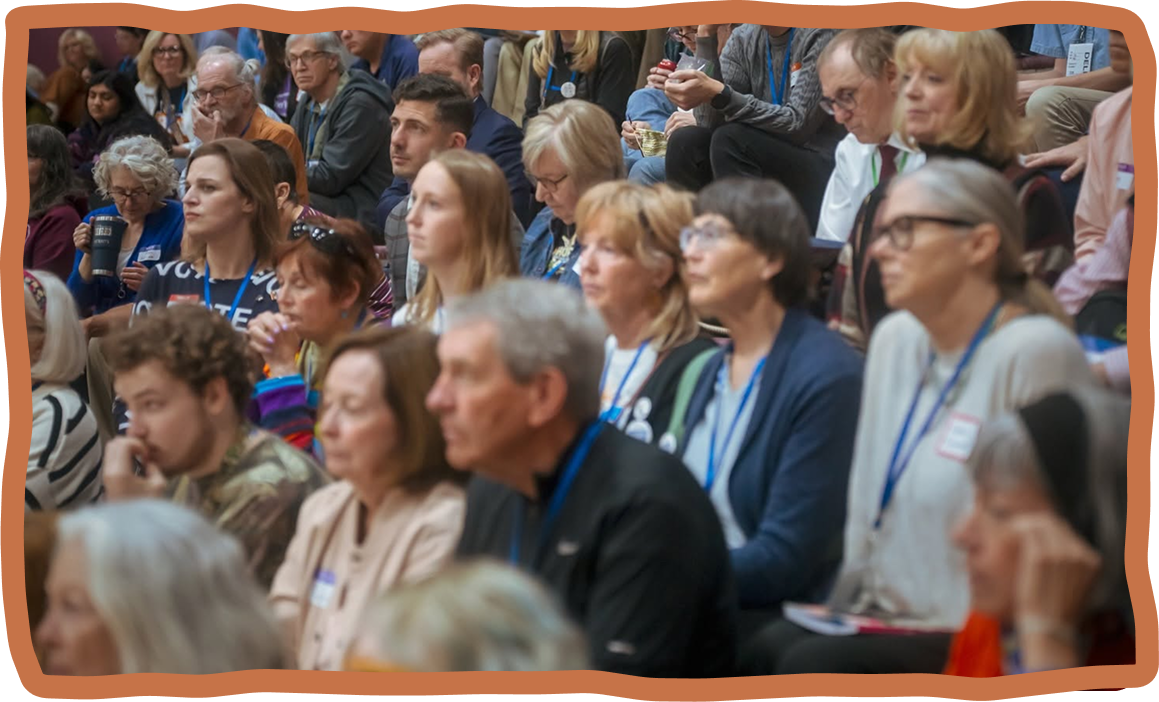 Audience attending a conference, seated in a large auditorium, attentively listening to a speaker.