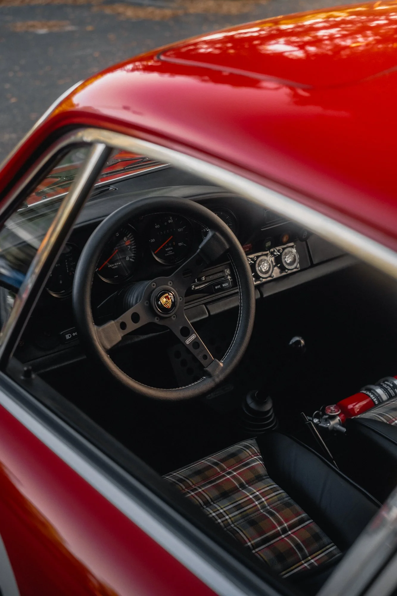 The interior of a vintage red G-Body Porsche 911 car showing the dashboard, steering wheel, and plaid-patterned seats.