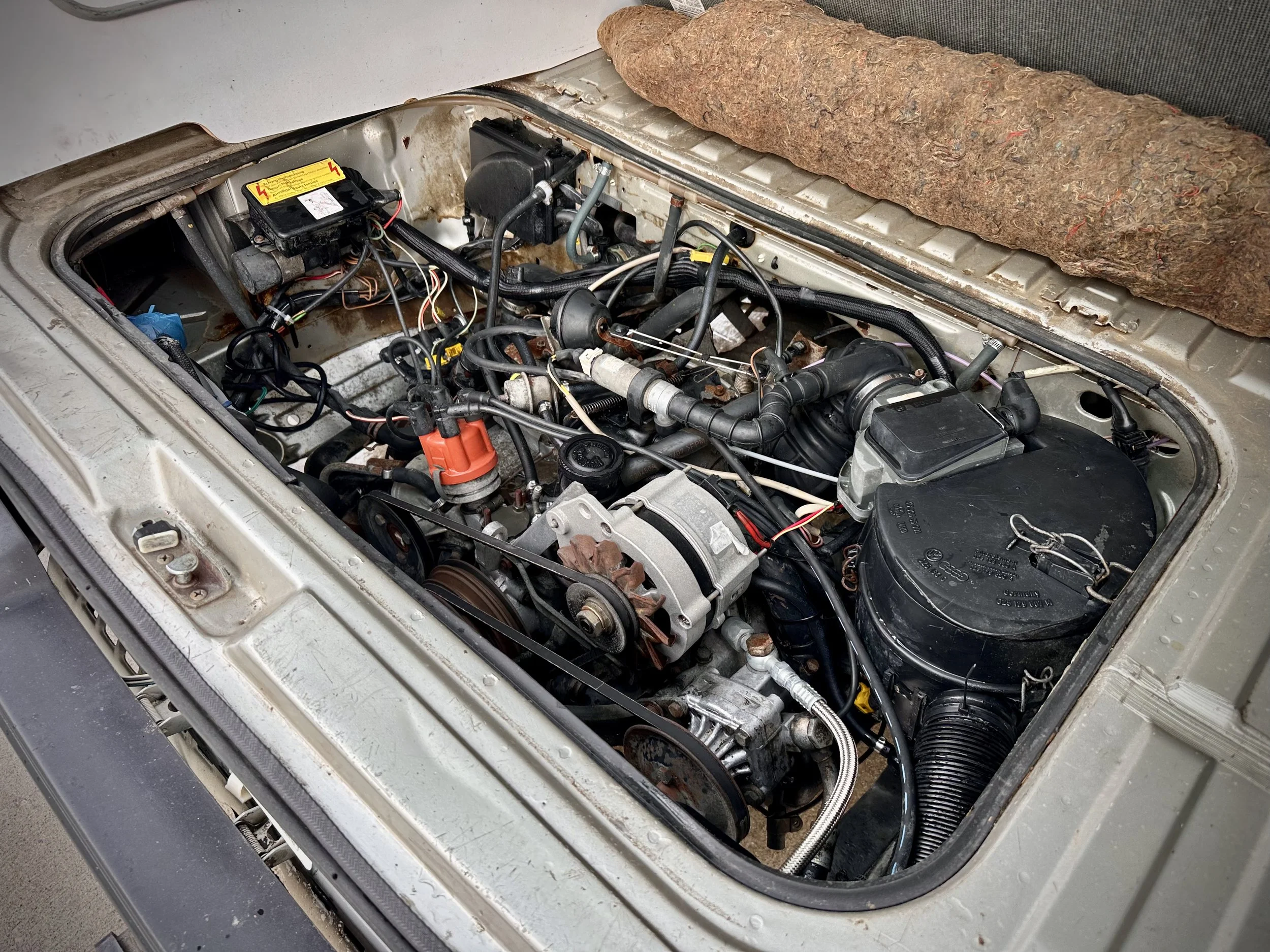 Vanagon engine bay with various engine components and wiring visible, with a felt-like material placed on top of the hood.