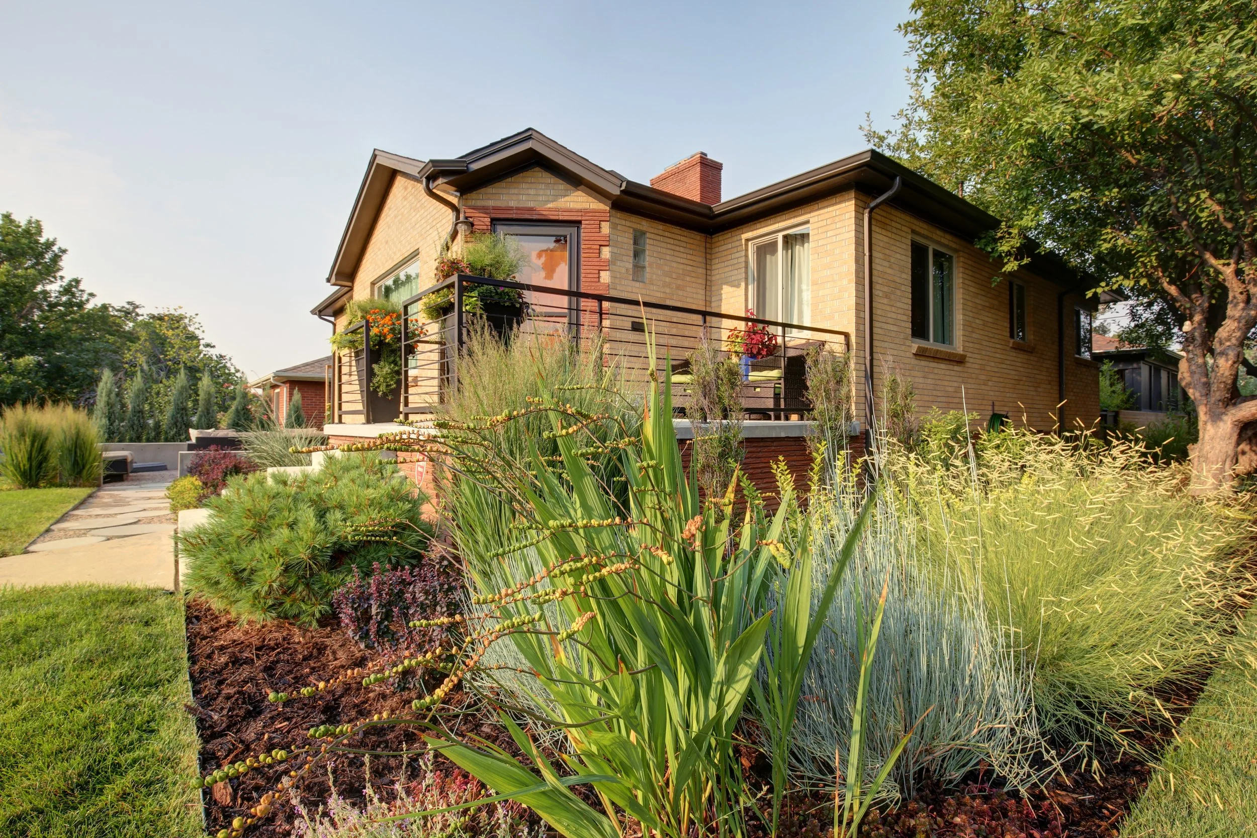 Brick home with landscaped yard and raised patio in Denver, designed by The Green Fuse with modern plantings.