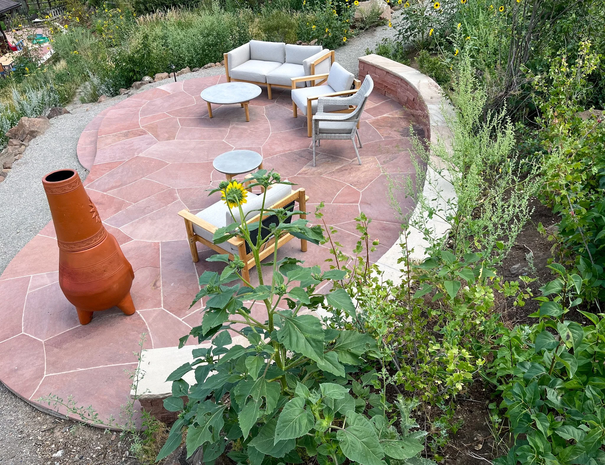 Outdoor stone patio with cushioned chairs, round tables, and a terracotta chiminea surrounded design by The Green Fuse of Denver, CO