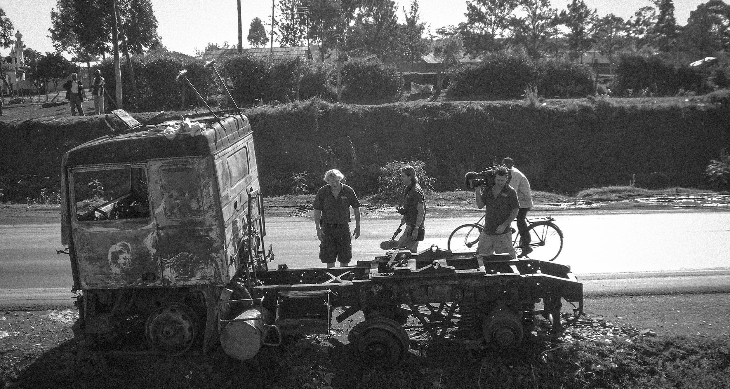 Documentary photograph of cinematographer Adam Docker, veterinary surgeon Luke Gamble and producer Marc inspecting a burnt-out vehicle following Kenya's 2007–08 post-election violence