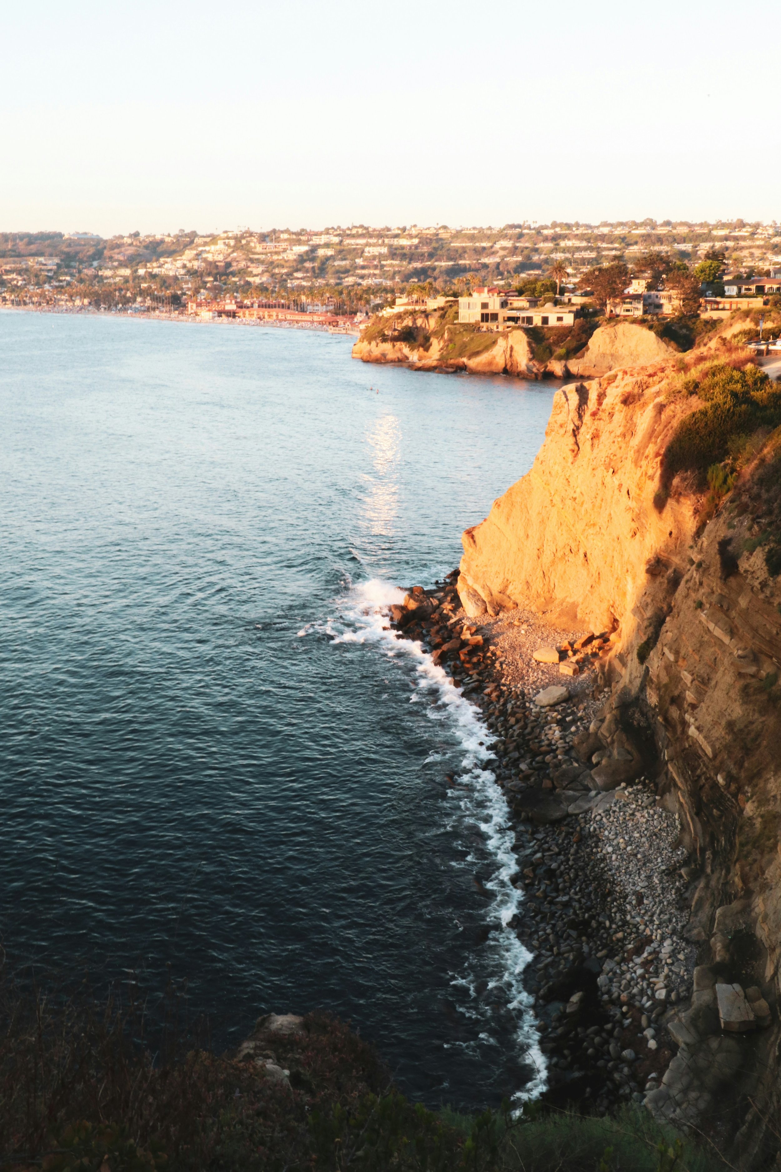 Sunset over the ocean with rugged cliffs and residential houses in the background