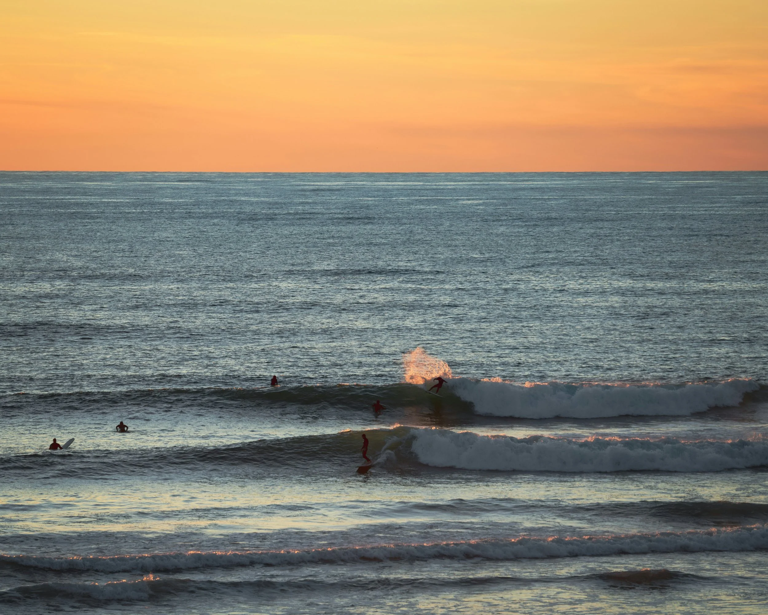 Sunset over the ocean with surfers riding waves.