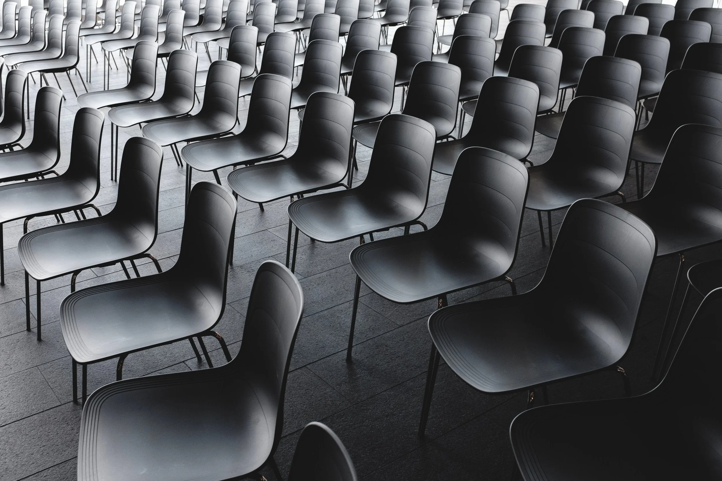 Multiple black chairs arranged in rows in a large, empty conference or event room.
