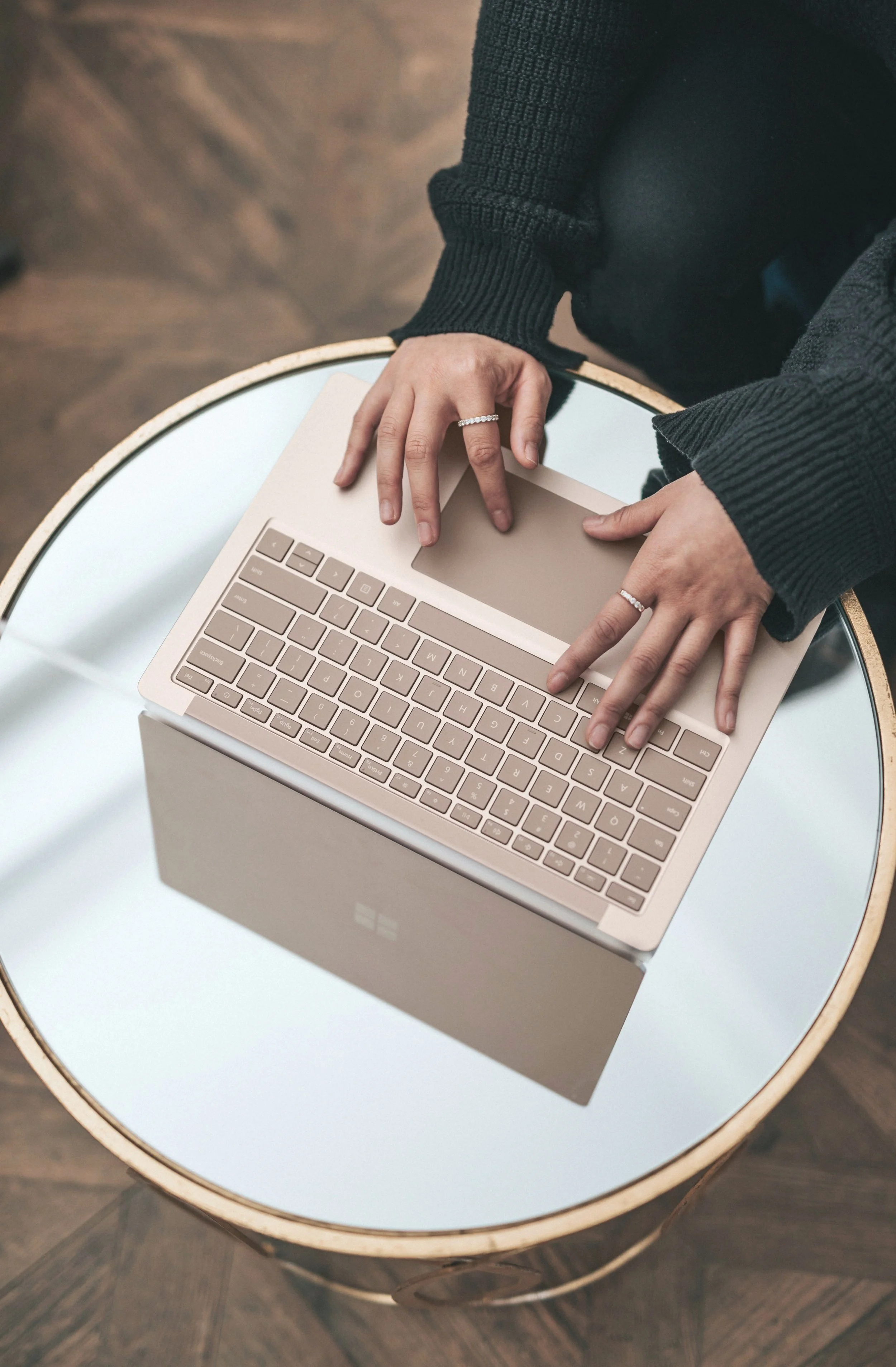 Person using a pink laptop on a round table with a mirrored surface.
