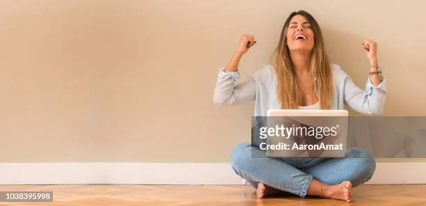 A young woman sitting cross-legged on the floor, smiling and raising her fists in celebration.