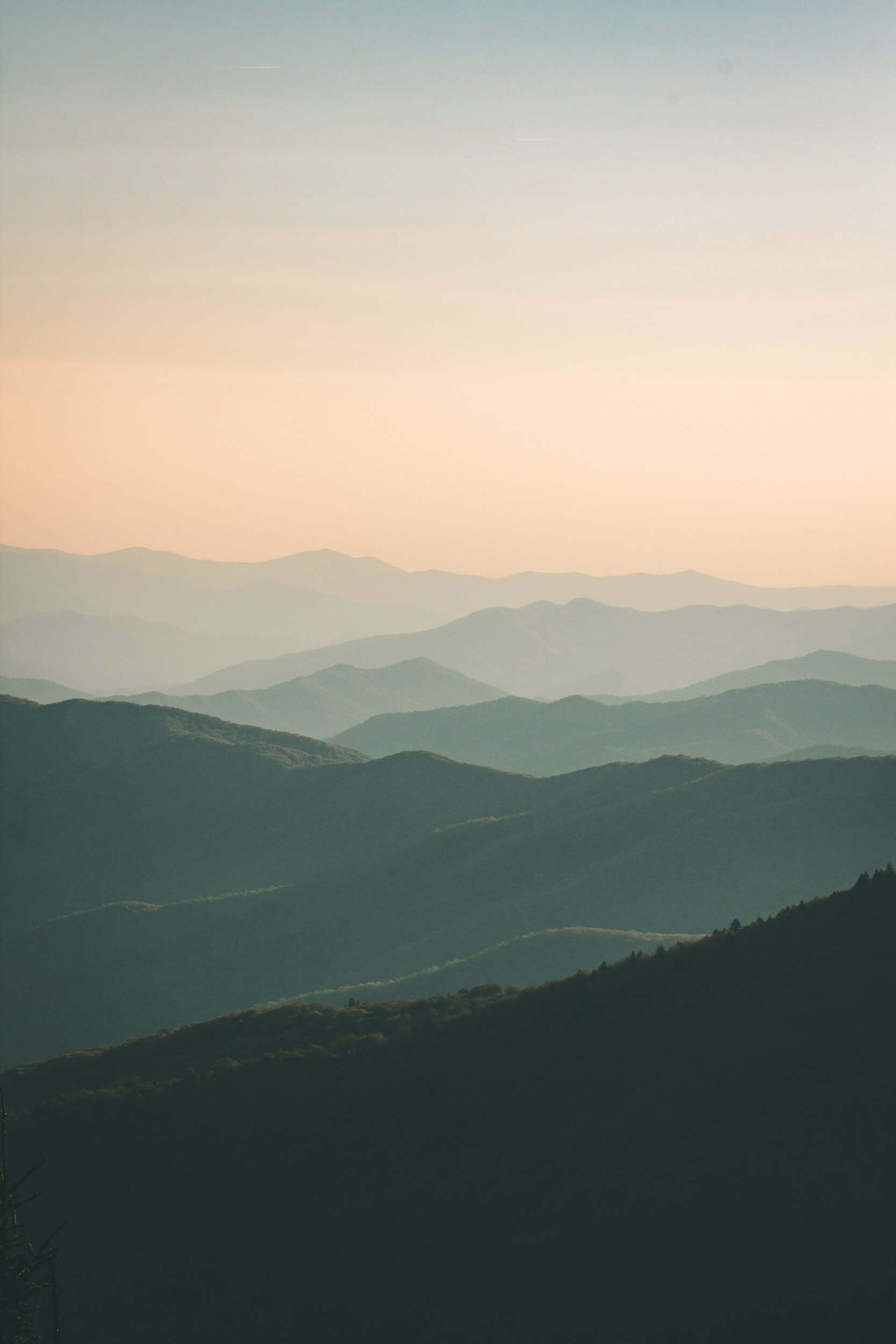 Layered mountain ranges under a pastel sky at sunrise or sunset.