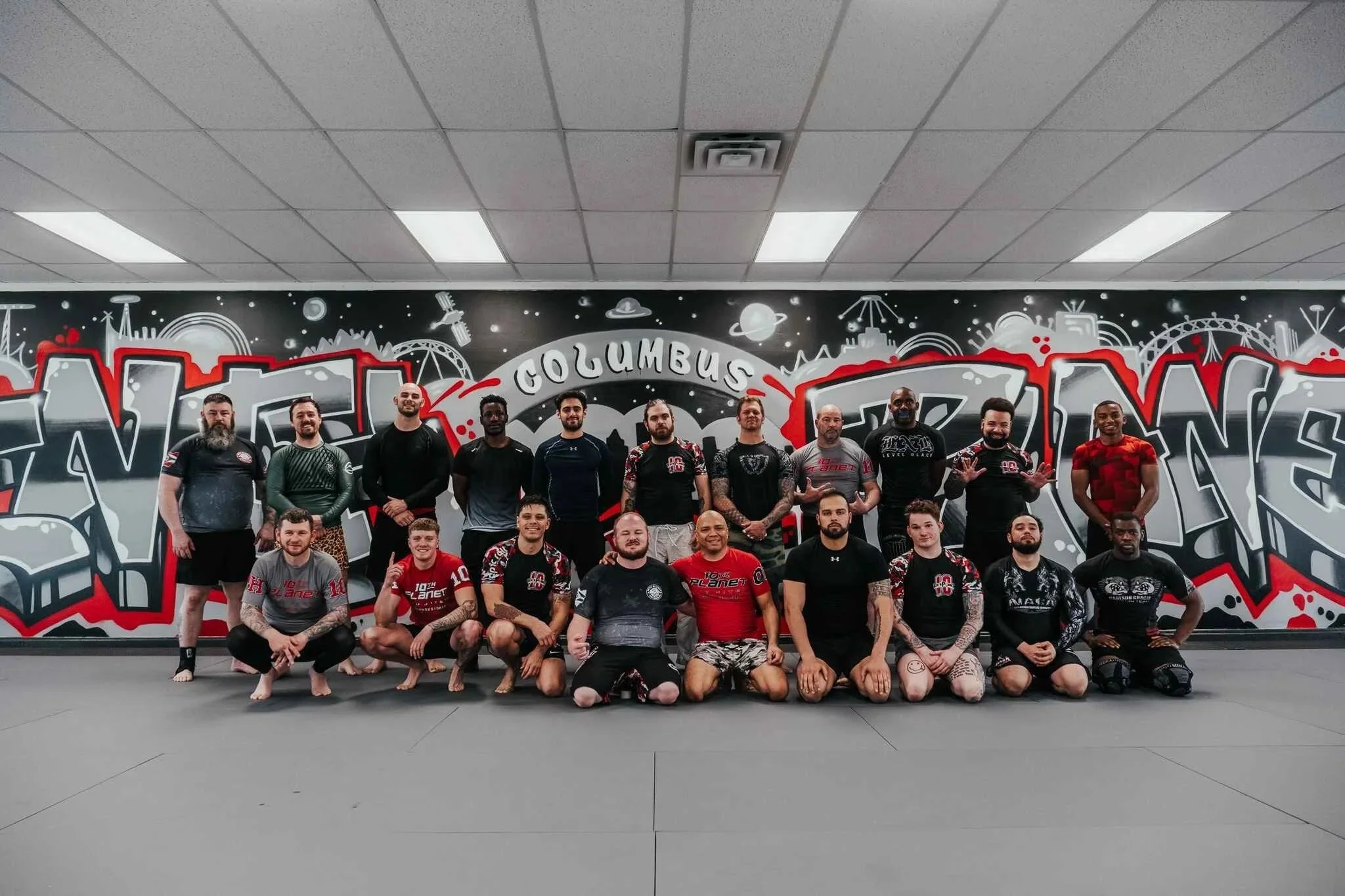 Group of individuals in martial arts uniforms posing in front of a graffiti-style wall that reads 'Columbus' and 'Martial Arts'.