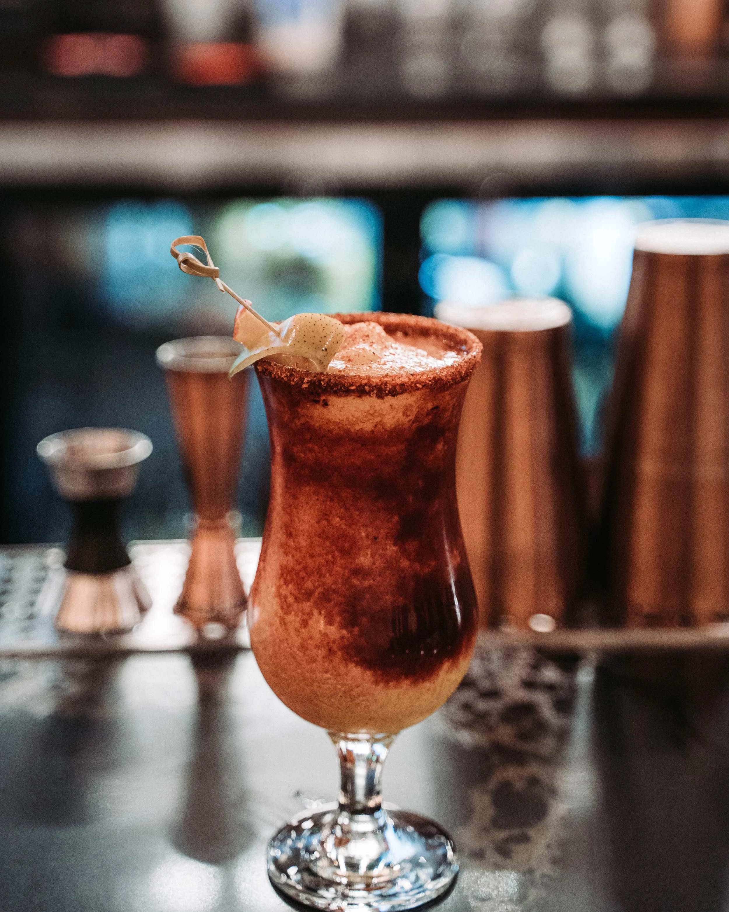 Mangonada with a spiced rim and garnish skewer in a tall glass at the bar