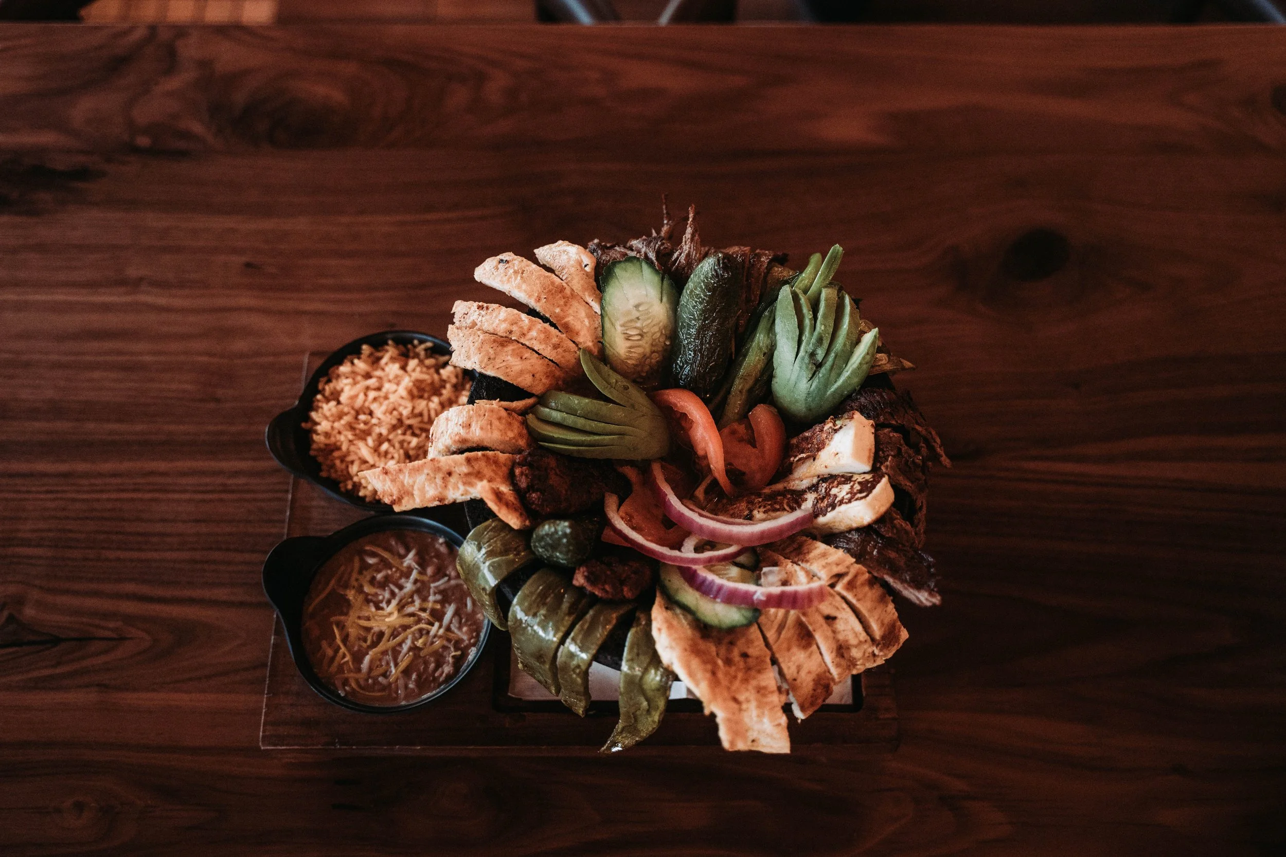Overhead view of a molcajete with sliced grilled meat, avocado, tomato, and cucumber, plus rice and beans