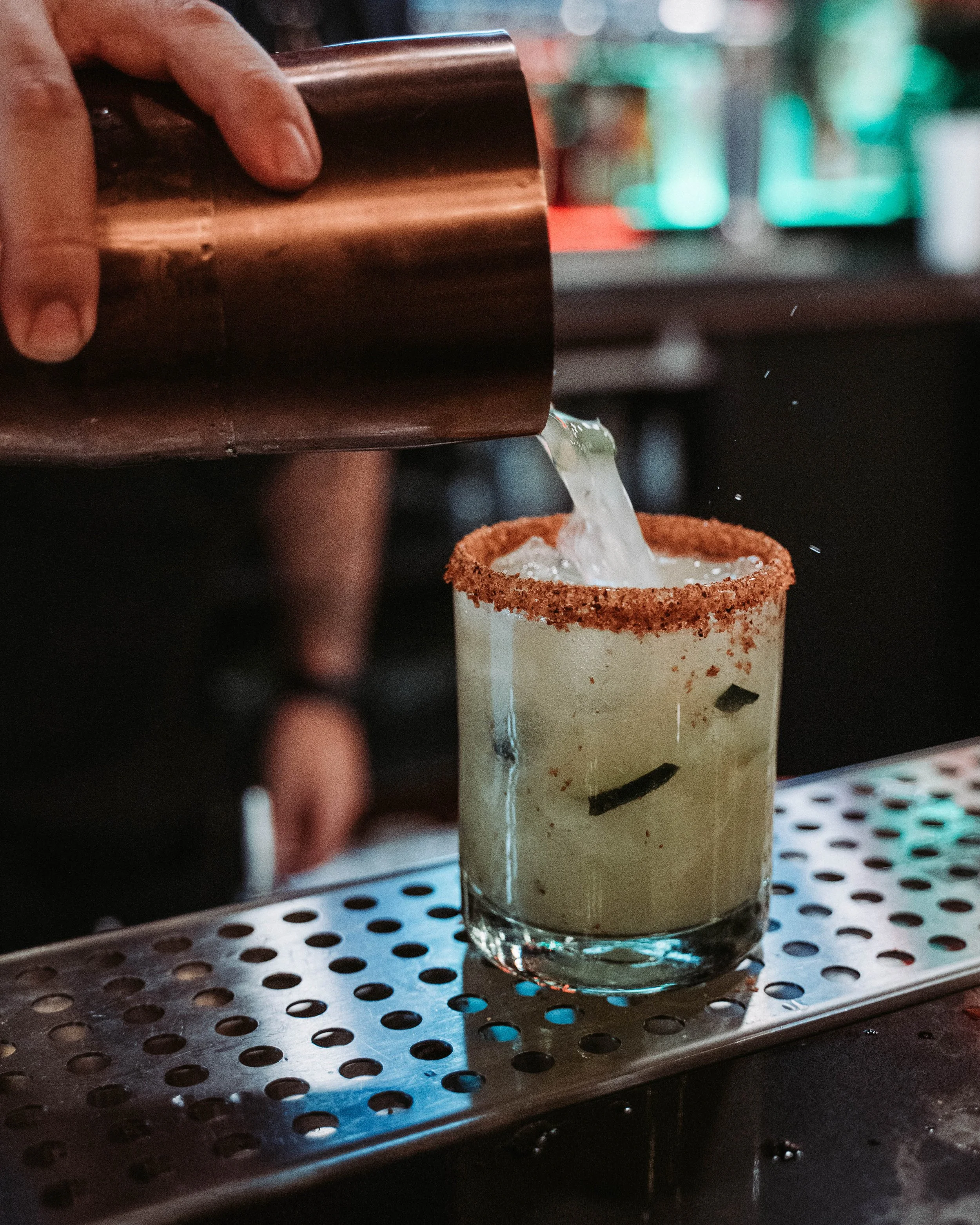 Bartender pouring a cucumber margarita with a chili-salt rim over ice