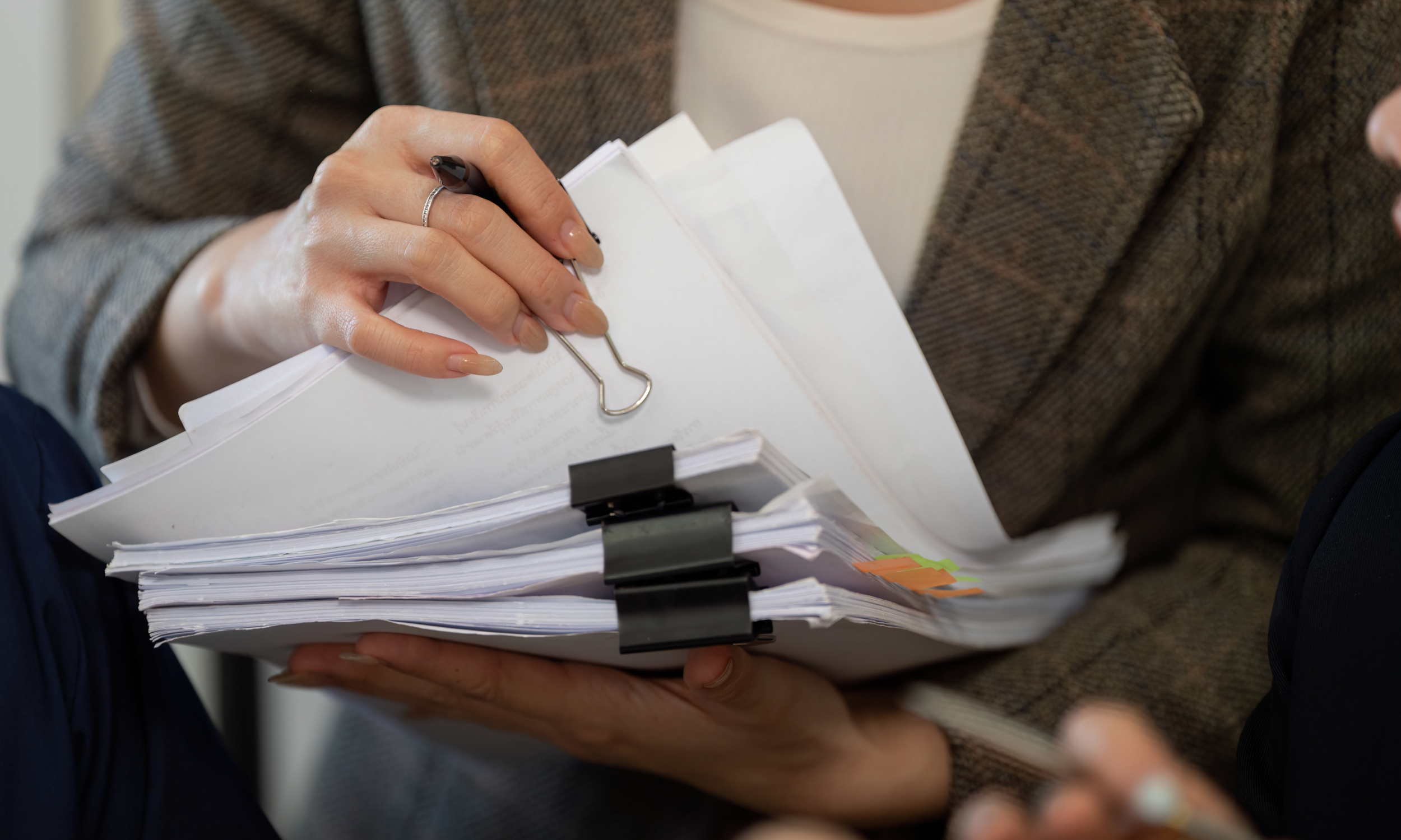 Person holding a stack of papers clipped with black binder clips, with a paperclip attached to the top sheet.