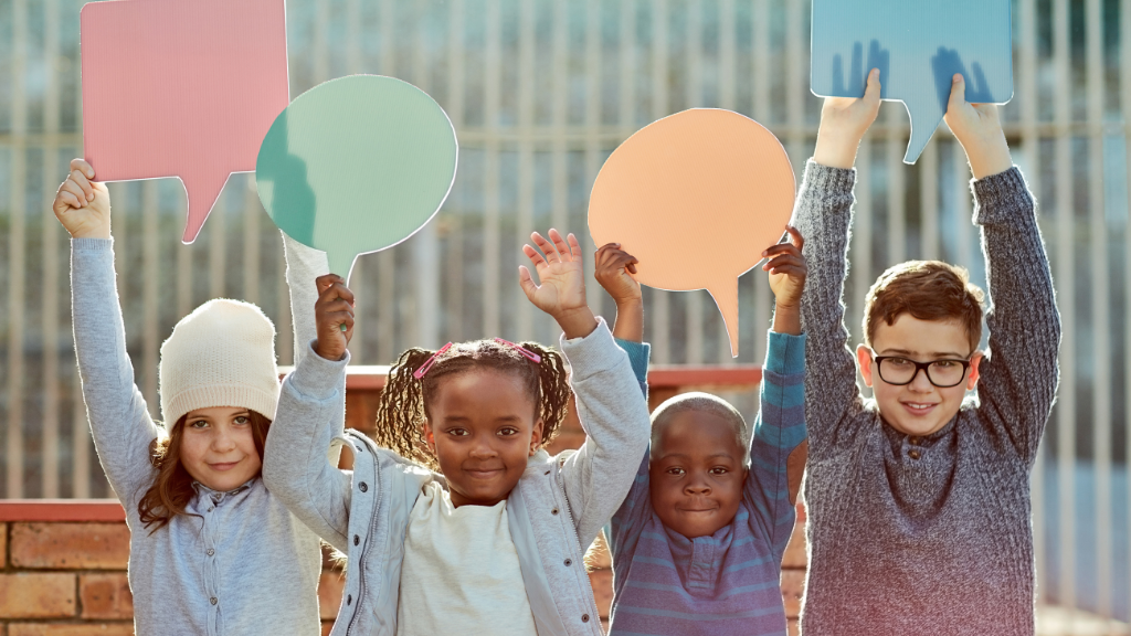 Four children holding up colorful speech bubble signs outdoors.
