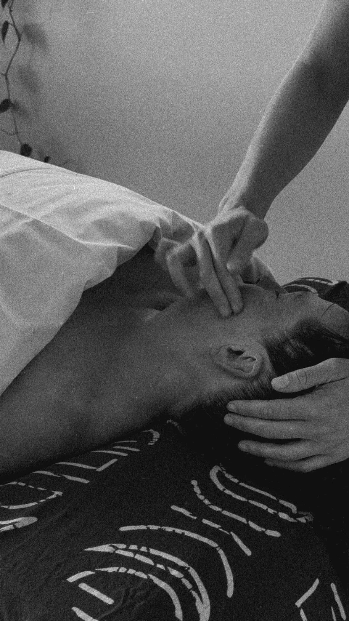 A person lying down with their head resting on a surface, receiving a gentle massage or medical treatment on their neck or face by another individual using their fingers.
