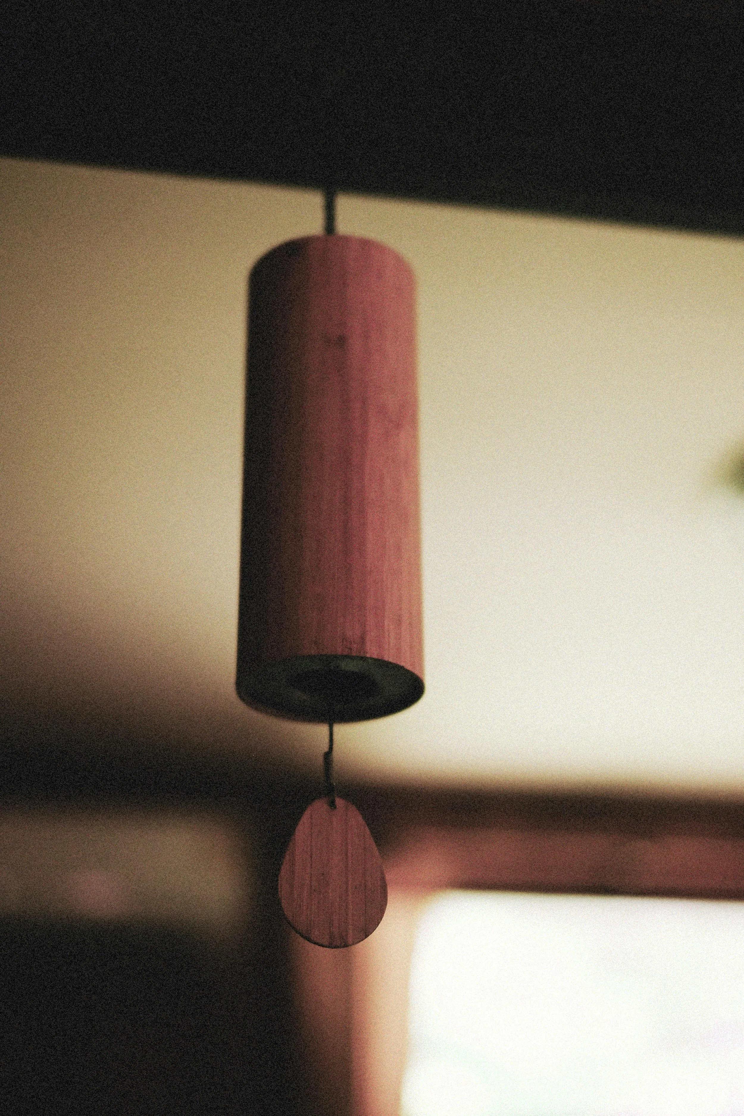 Close-up of a hanging wooden wind chime with round, flat, reddish-brown wooden elements hanging from a thin string against a blurred background.