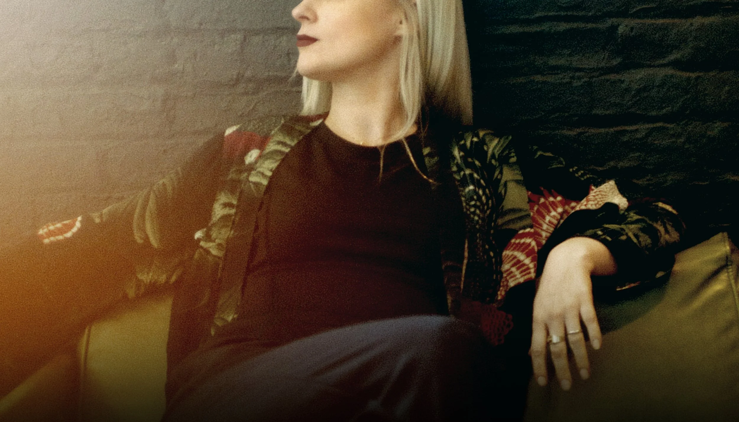 Moody, dark-color image of Quinn sitting on a vintage green leather couch.