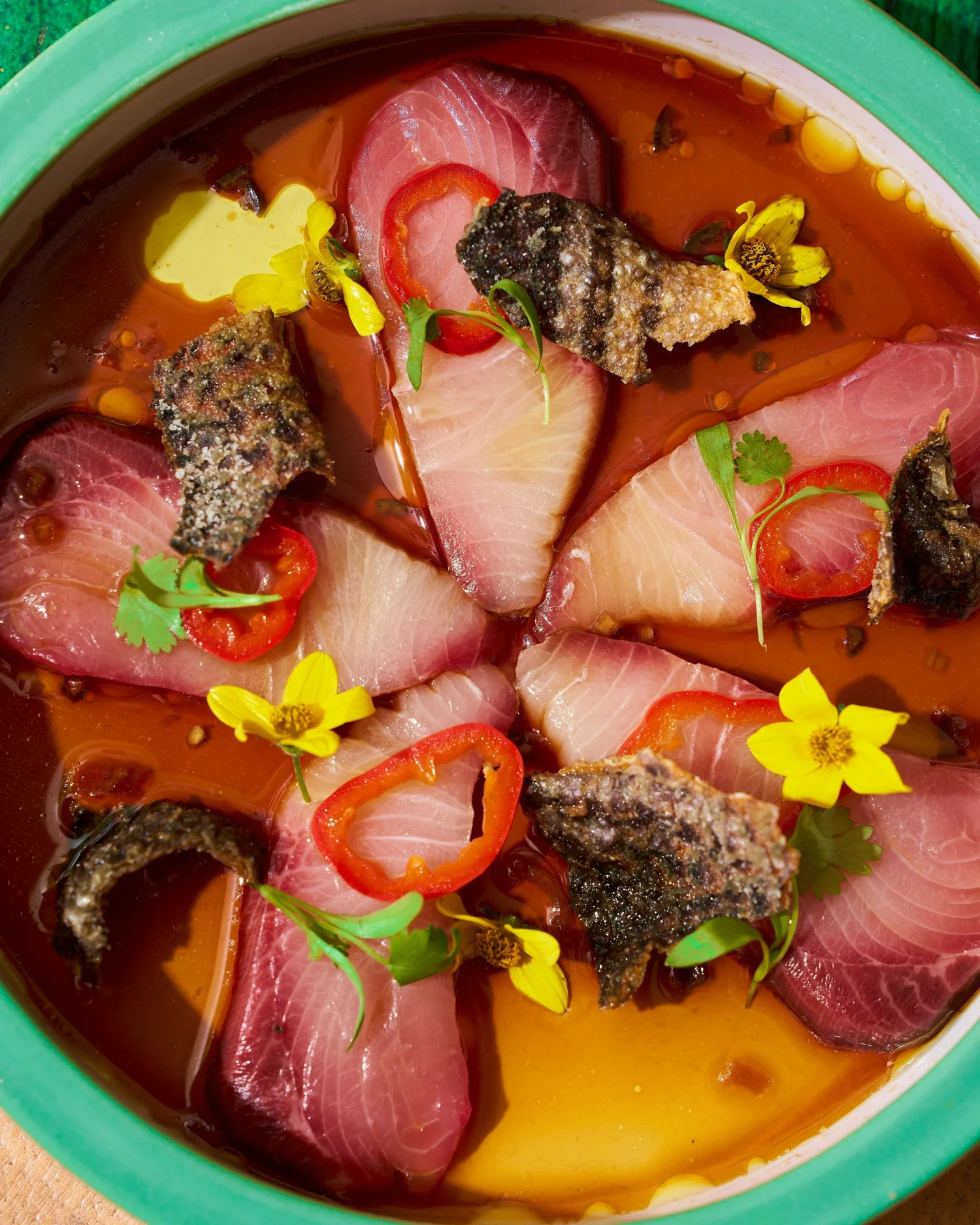 Crudo with crispy fish skin, chili and edible flowers in a green bowl