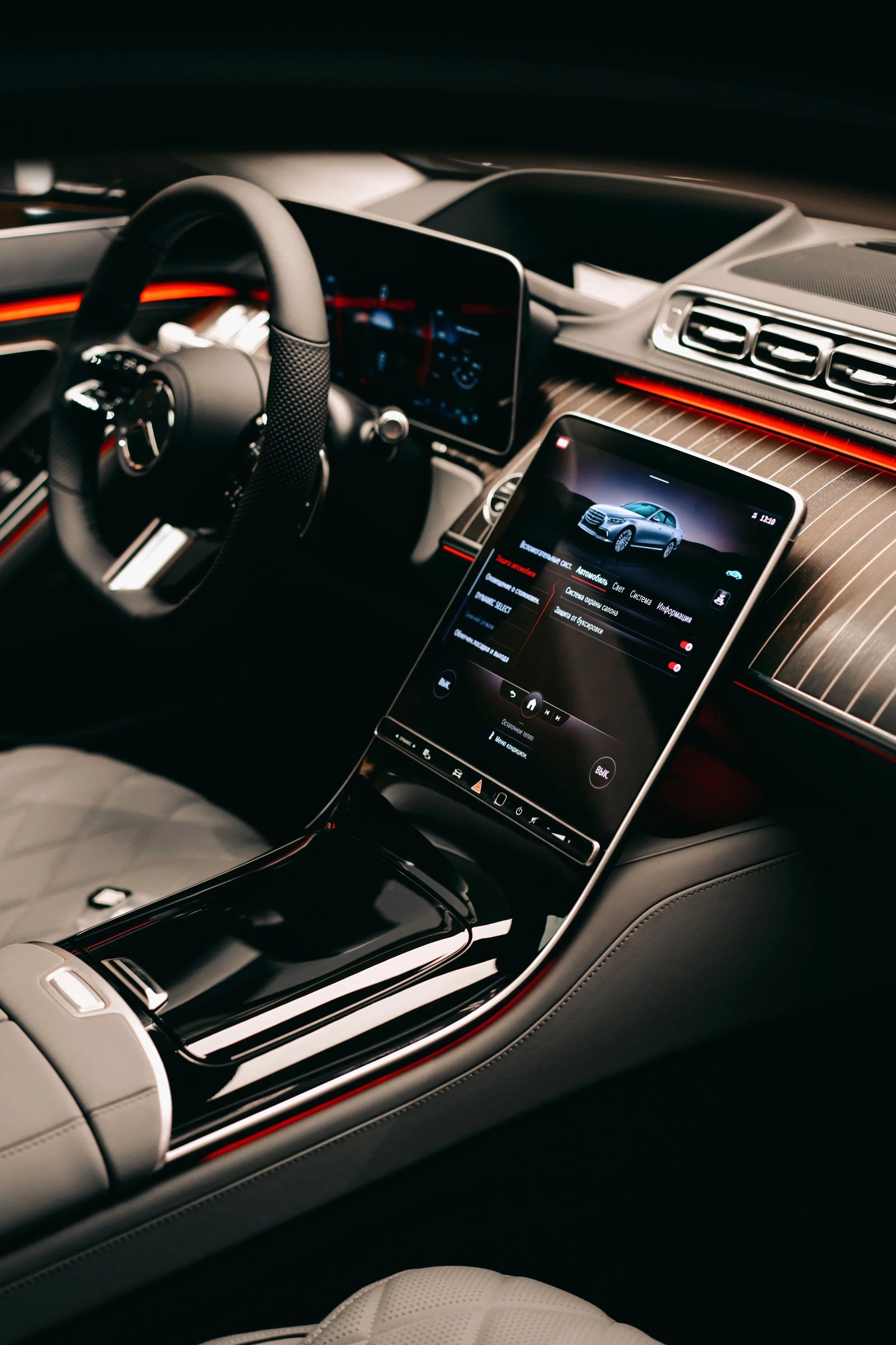 A modern car interior featuring a steering wheel, digital dashboard, a central touchscreen display showing a car graphic, and air conditioning vents with ambient lighting.