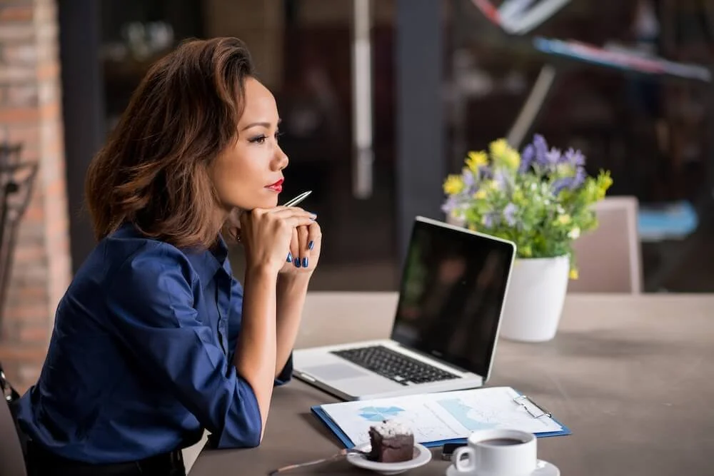 Woman sitting beside her laptop, pausing to reflect during the workday.