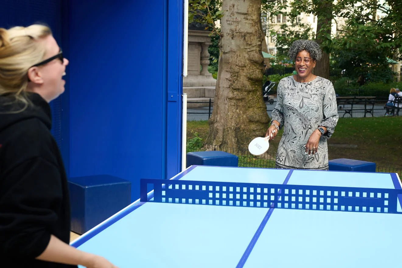 Two Women Laughing while playing table tennis at IBM's space cube installation in Madison square park 