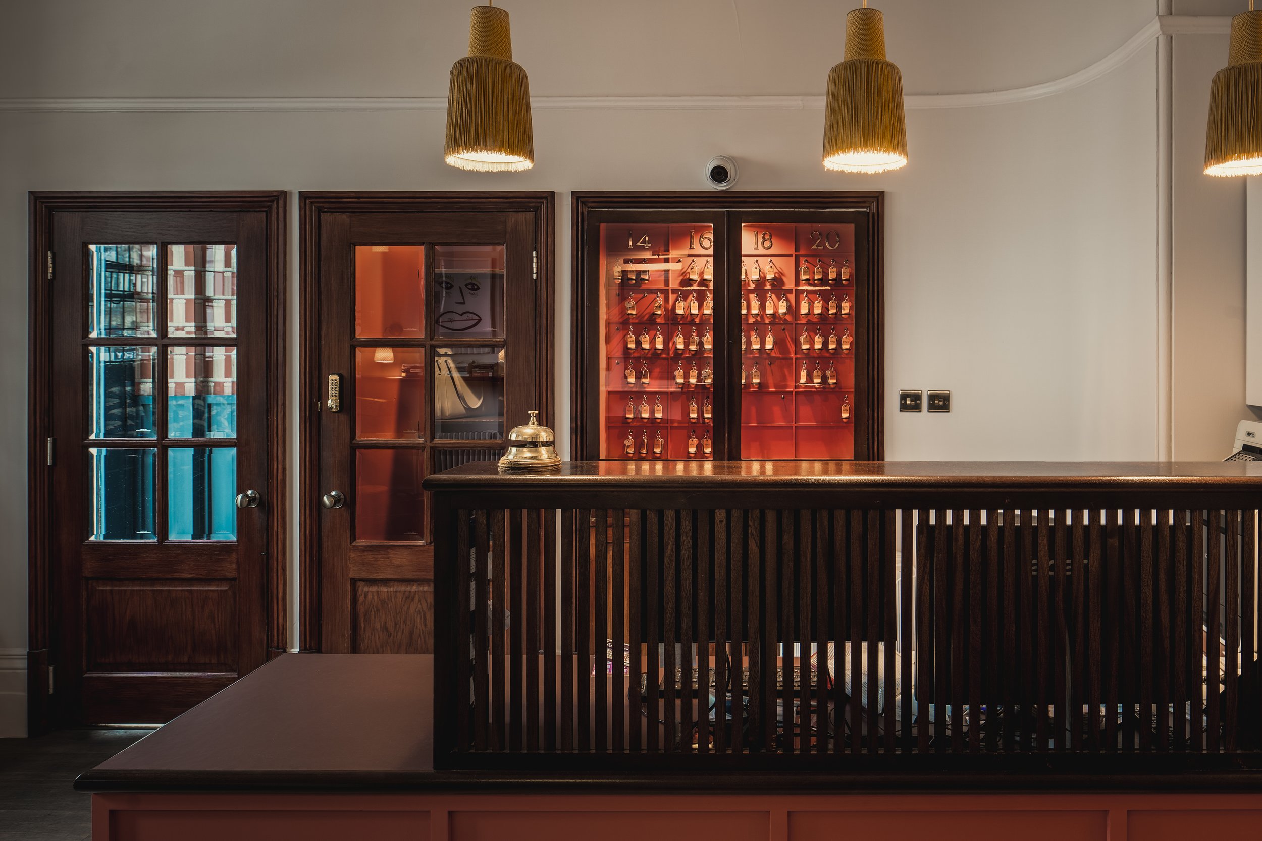 A bar counter with a bell on top, wooden doors with glass panels, a display cabinet with bottles numbered 14 to 20, and hanging pendant lights.