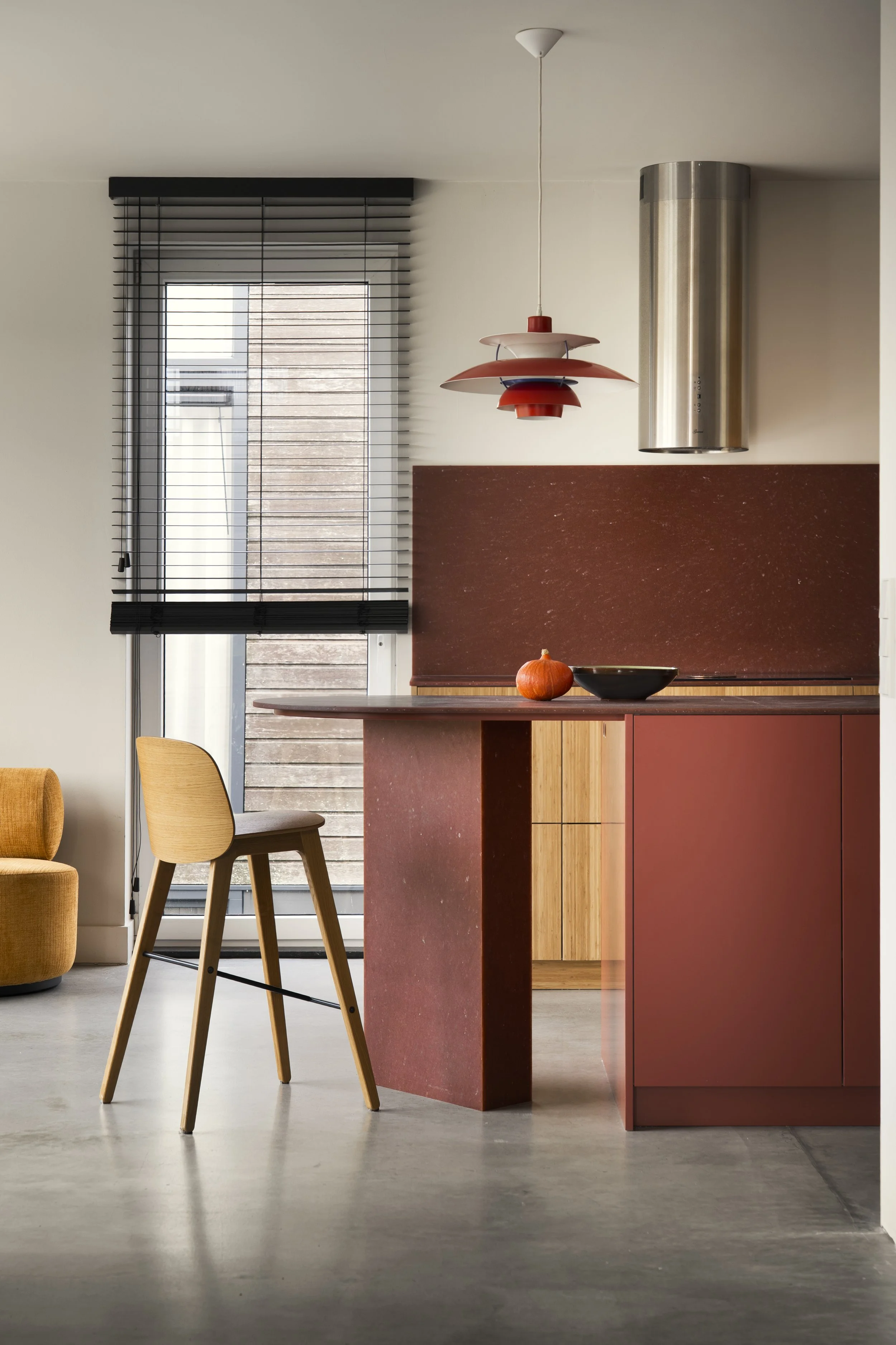 Modern kitchen with a saturated red island,bamboo kitchen cabinetry, a design classic light fixture, a large window with black blinds, and a stainless steel range hood.