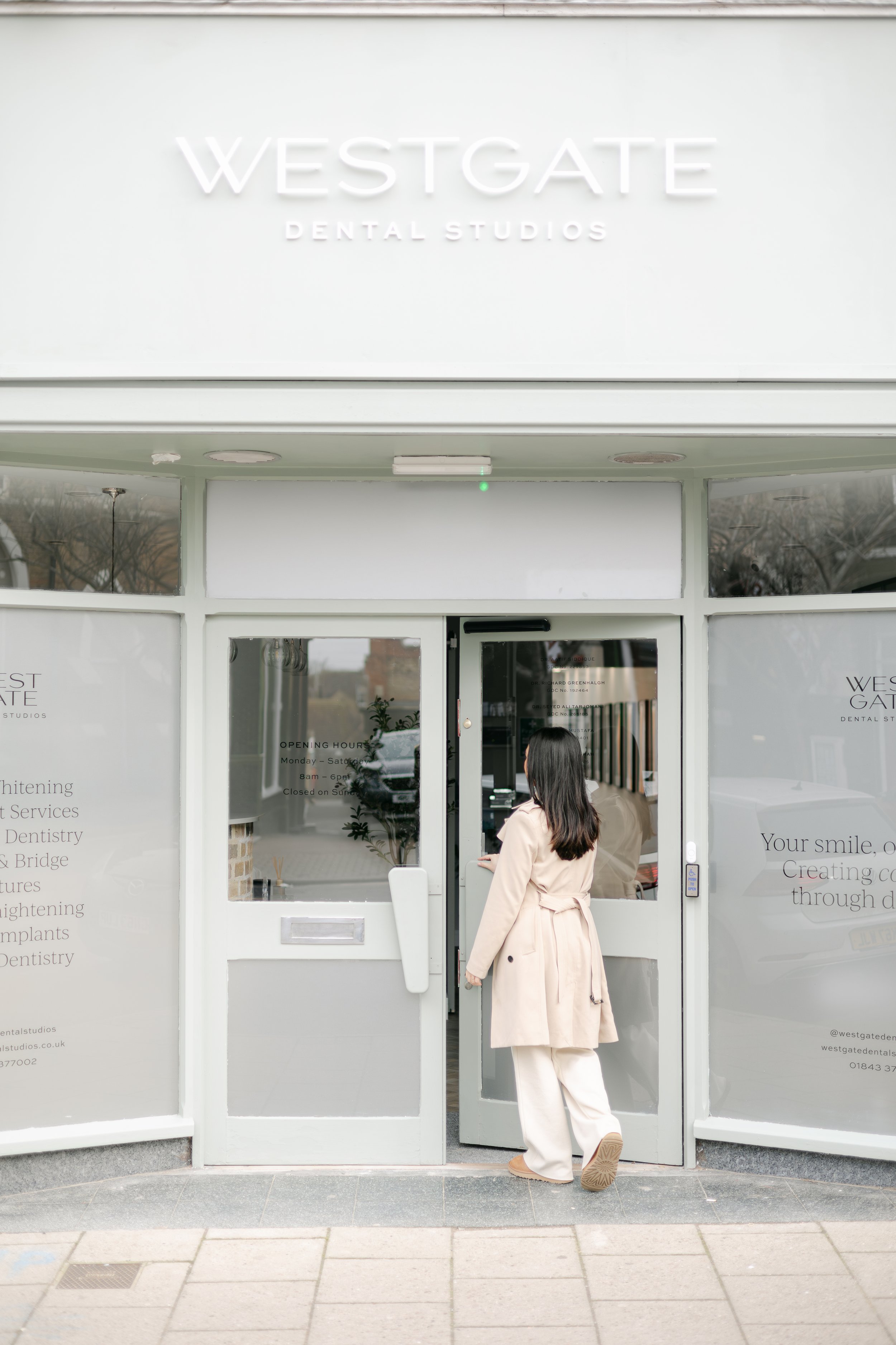 Woman entering a dental office called Westgate Dental Studios, located on a city street.