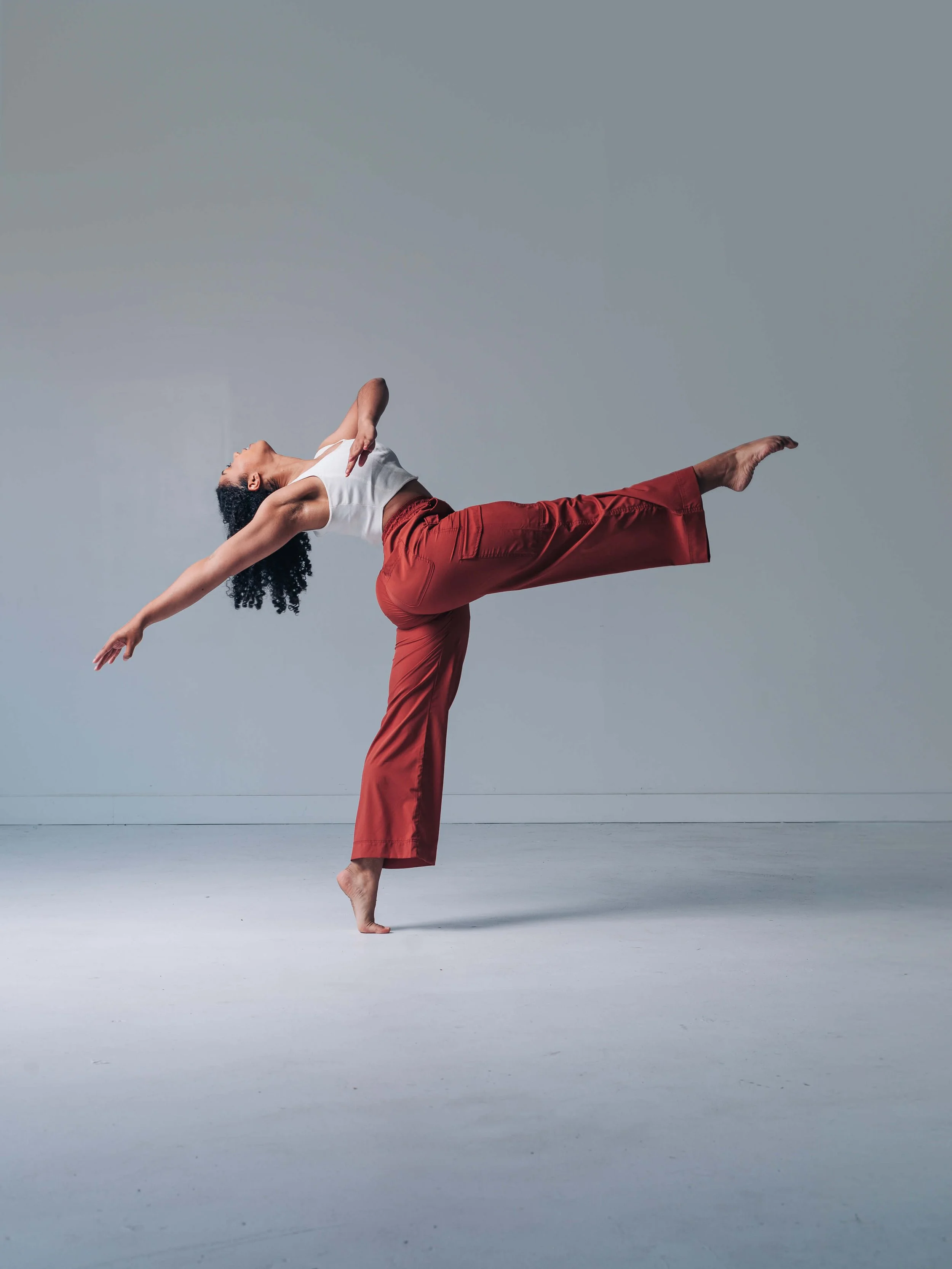 Elegant professional dancer in a white top and red pants performing a graceful pose with an arched back and extended leg, showcasing how to pose for dance photography.