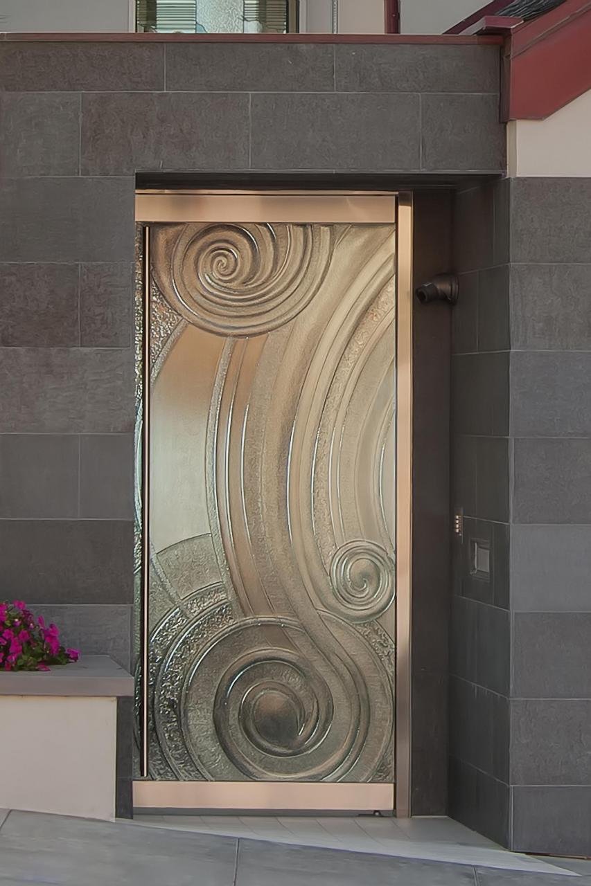 THE HOME’S HANDMADE FRONT DOOR IS MADE BY CARVING THE DESIGN IN SAND, WHICH THEN SERVES AS A MOLD FOR MOLTEN GLASS THAT IS POURED ONTO IT AND LEFT TO COOL.
