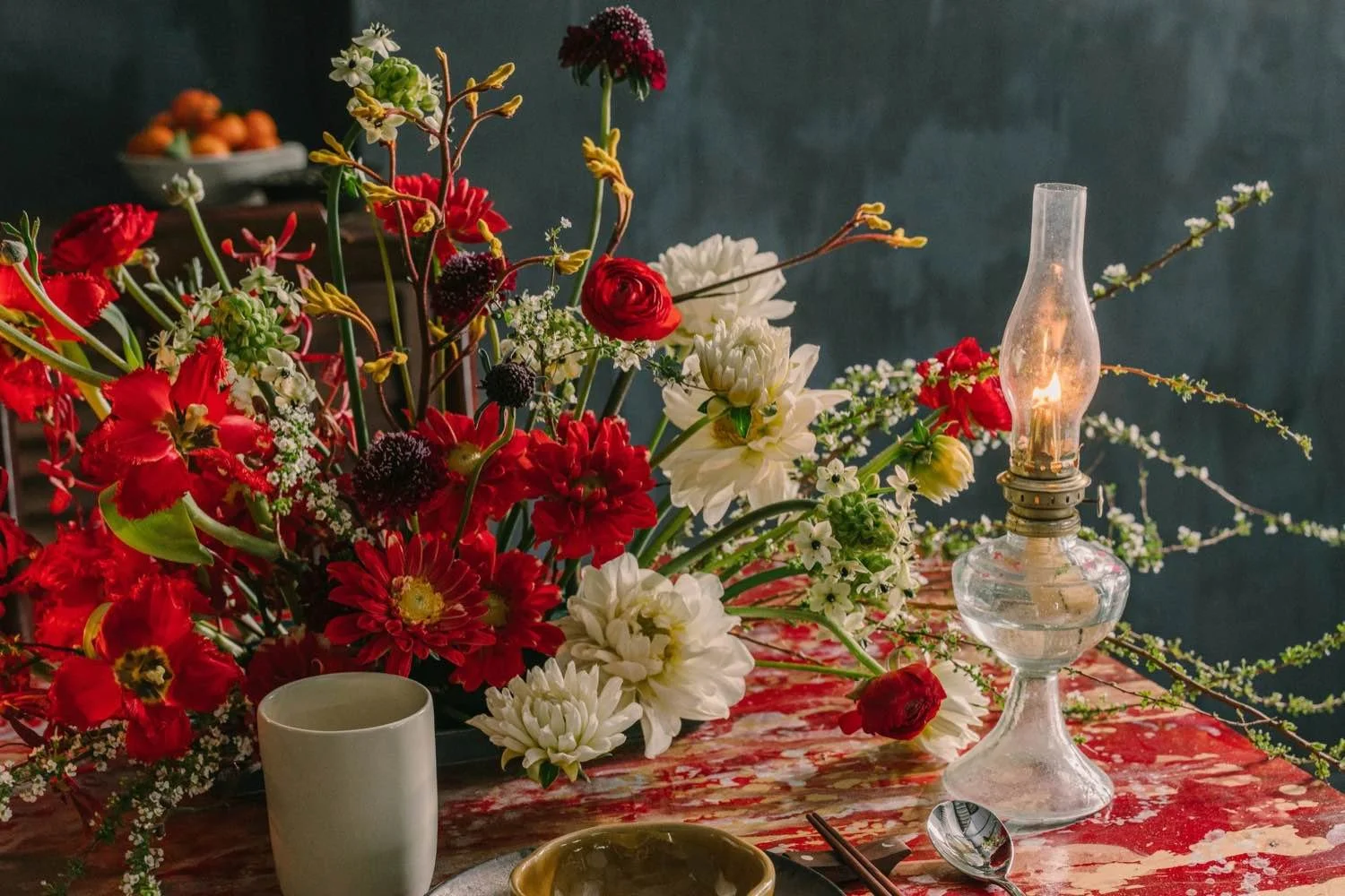 Red and white floral arrangement beside a glowing oil lamp