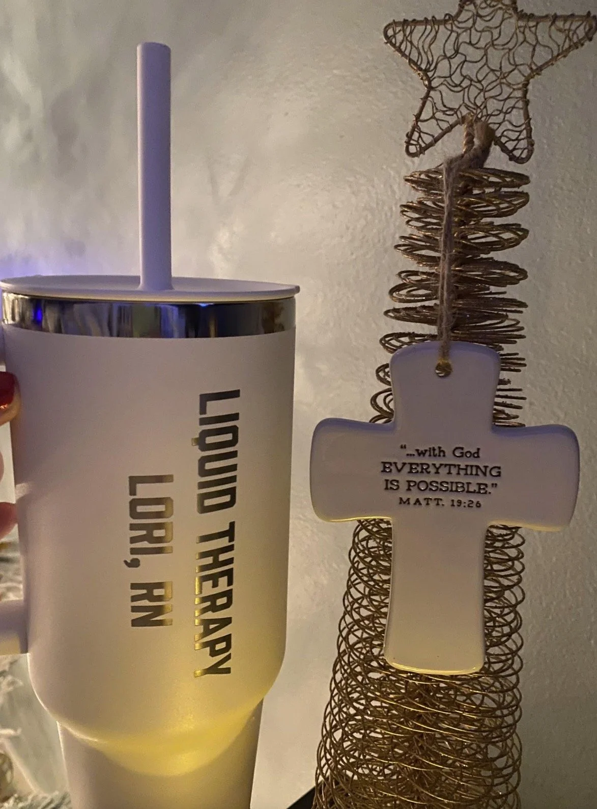 A white tumbler with a straw and a metallic rim, attached to a sign with the quote, 'With God EVERYTHING IS POSSIBLE.' Matthew 19:26, and a decorative wire star.