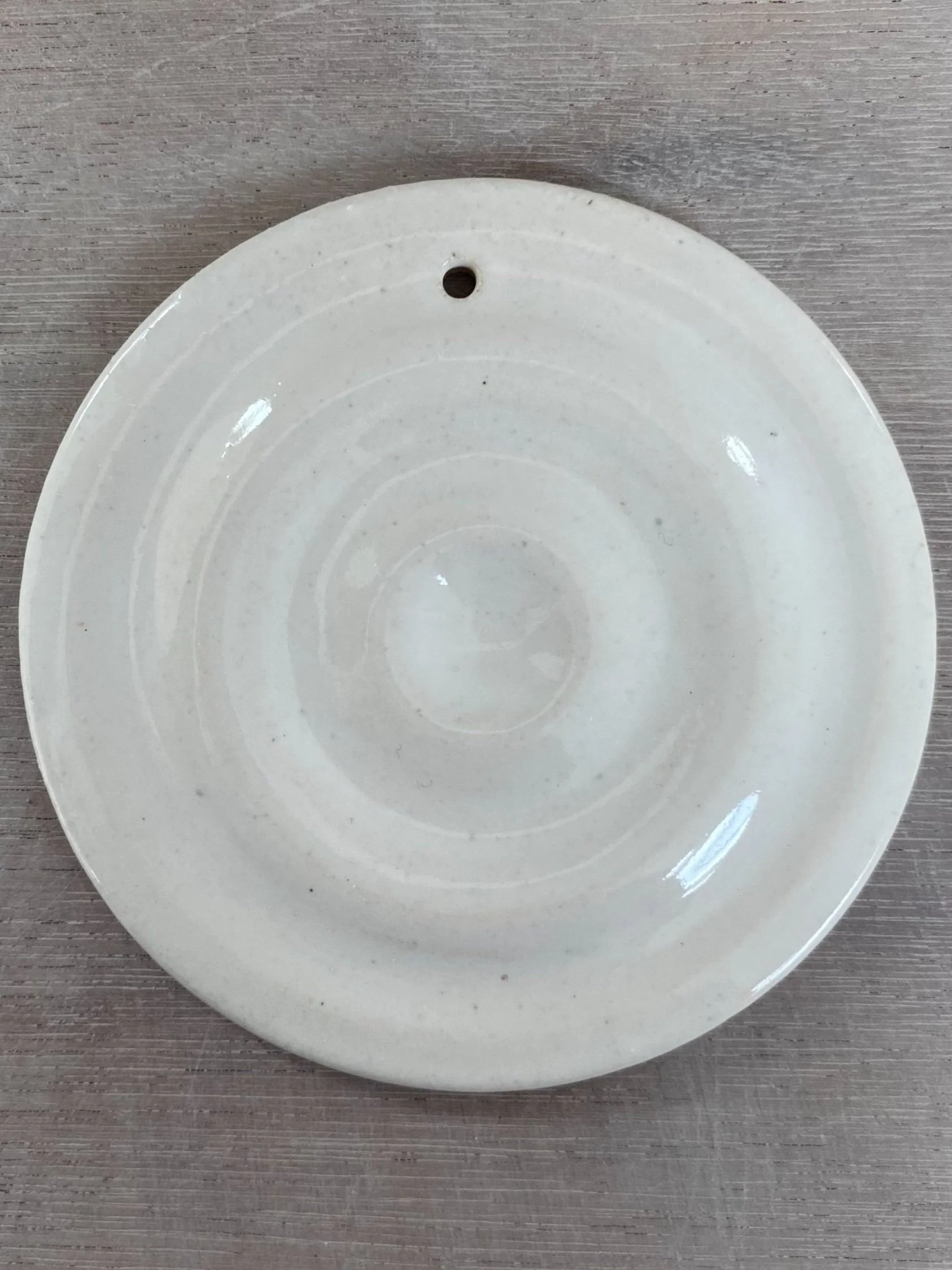 A plain white, round ceramic plate with minor specks and concentric ridges, placed on a wooden surface.