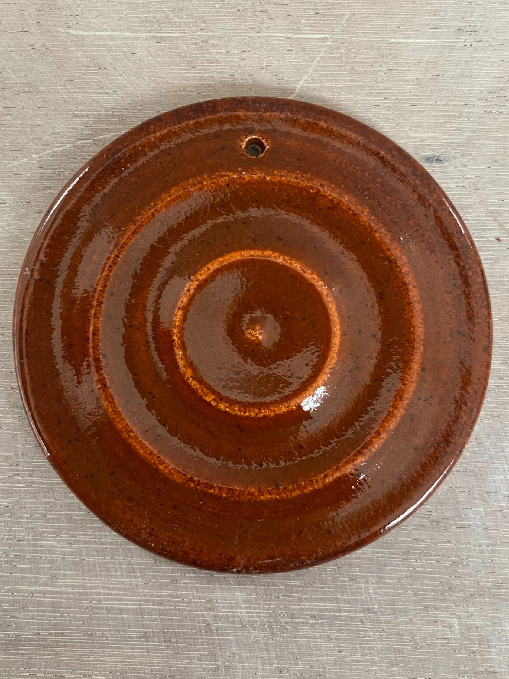 A round, rust-colored metal object with concentric circles and a small hole near the top, resting on a light-colored wooden surface.