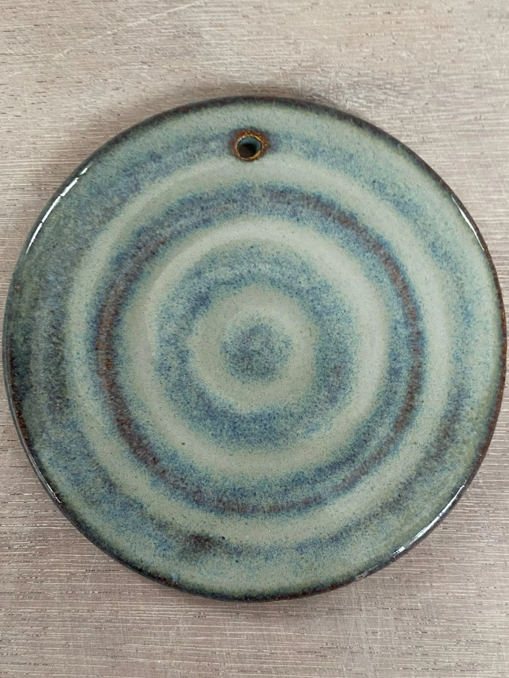 A round ceramic plate with a spiral pattern in green, blue, and brown hues, lying on a wooden surface.