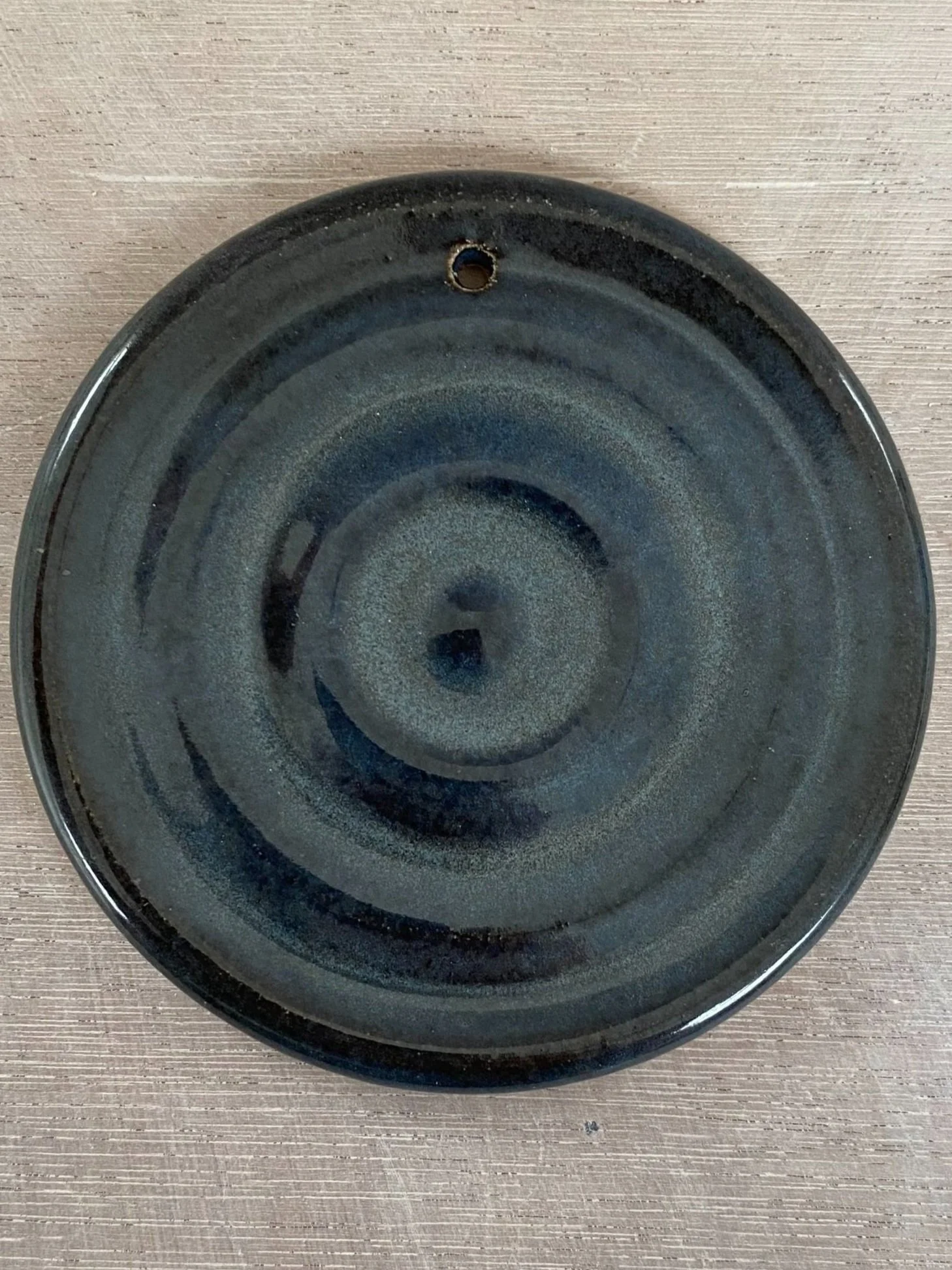 Round, black ceramic plate with a spiral design, resting on a light-colored wooden surface.
