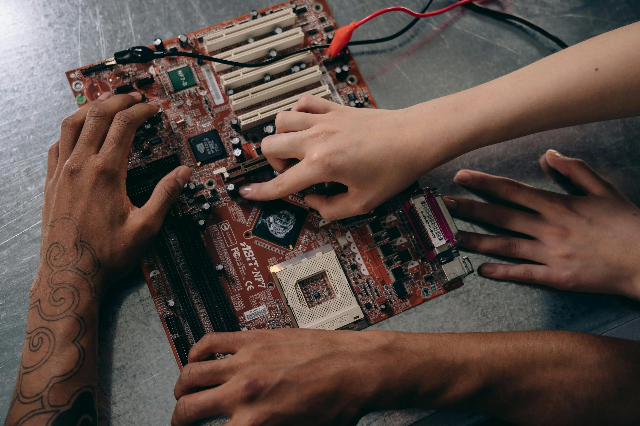 Hands working on a red computer motherboard placed on a gray surface.