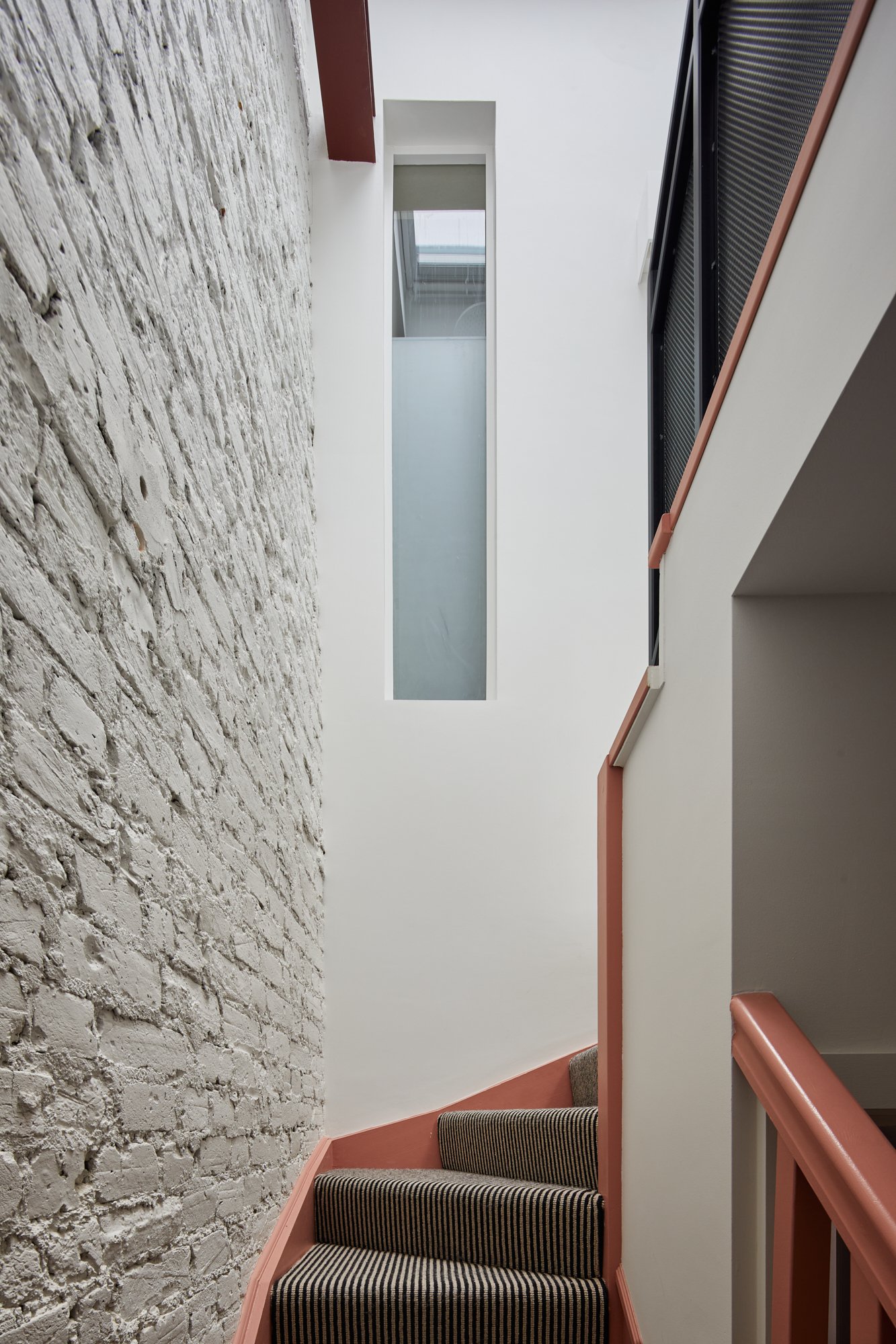 Exposed white brick wall with custom pink staircase and striped carpet, internal windows allow light to shine through London SW1V